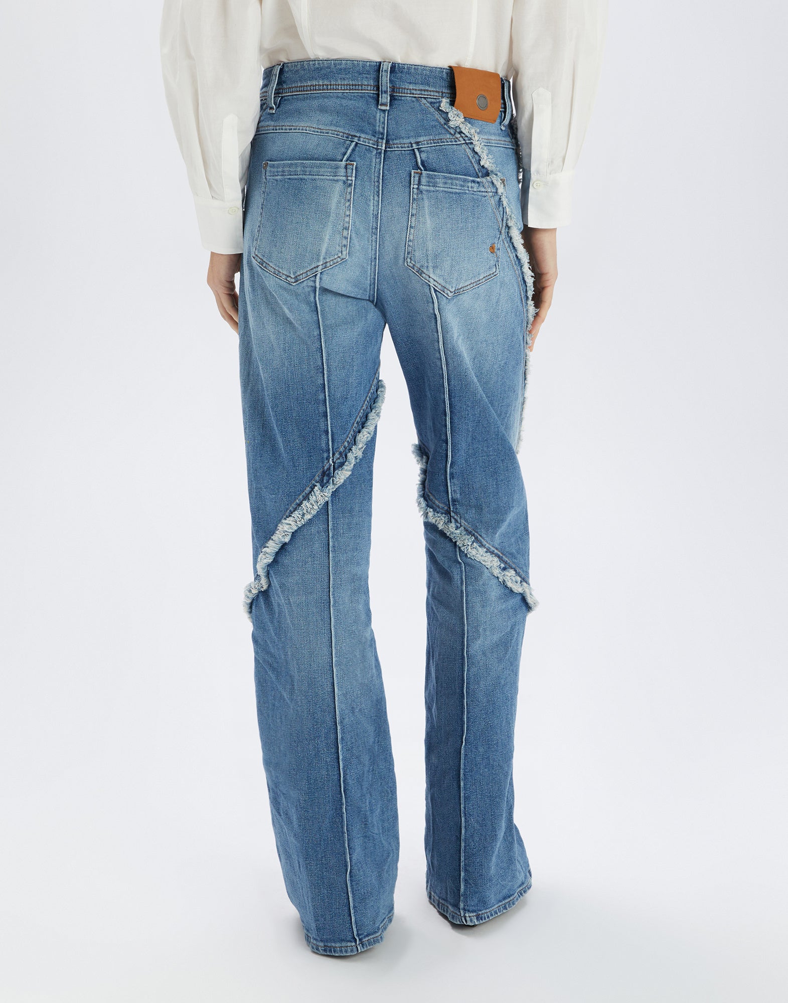 Rückansicht der INDULGE Jeans mit weitem Bein, ausgefransten offenen Nähten, zwei Gesäßtaschen und sichtbaren Steppungen in hellem Denim-Ton.