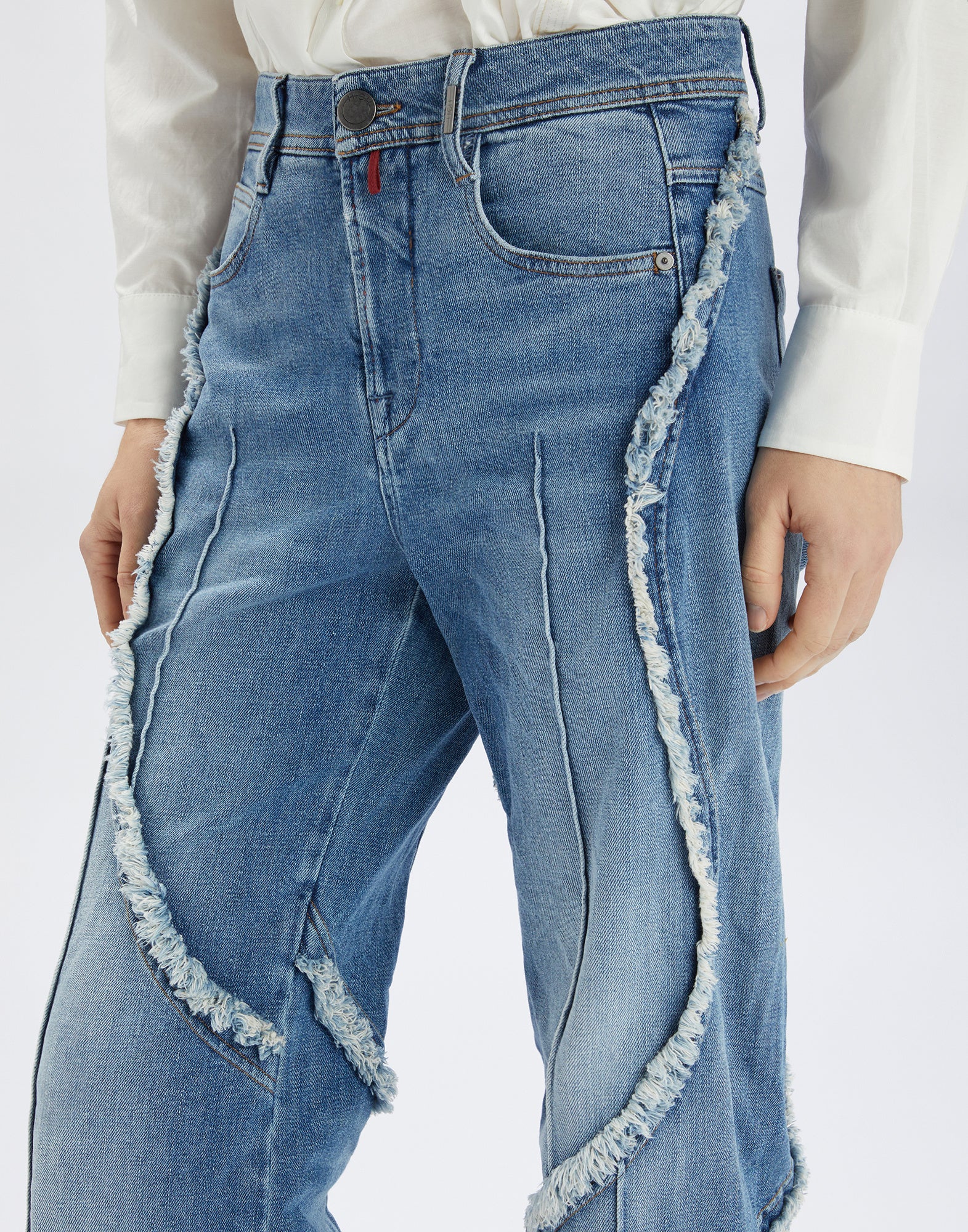 Frontalansicht der INDULGE Jeans mit ausgefransten Außenkanten, sichtbaren Nähten und weitem Bein. Heller Denim mit markanten Details, getragen mit Hemd.