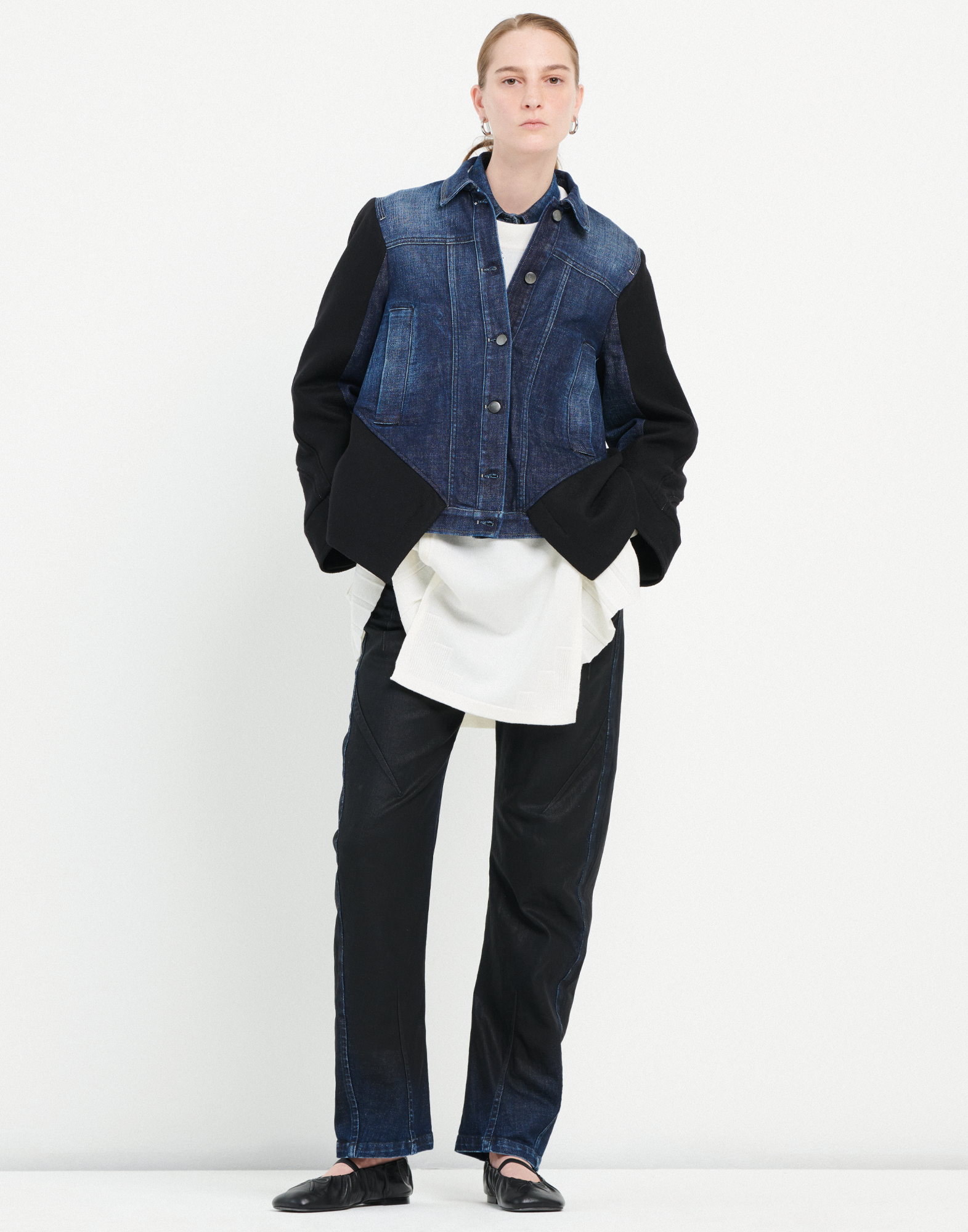 Frontalansicht einer Person, die die TRICE Jeans trägt; die Hose ist gerade geschnitten mit leichter Banana-Beinform, sichtbaren Nähten und dunkler, leicht glänzender Optik.