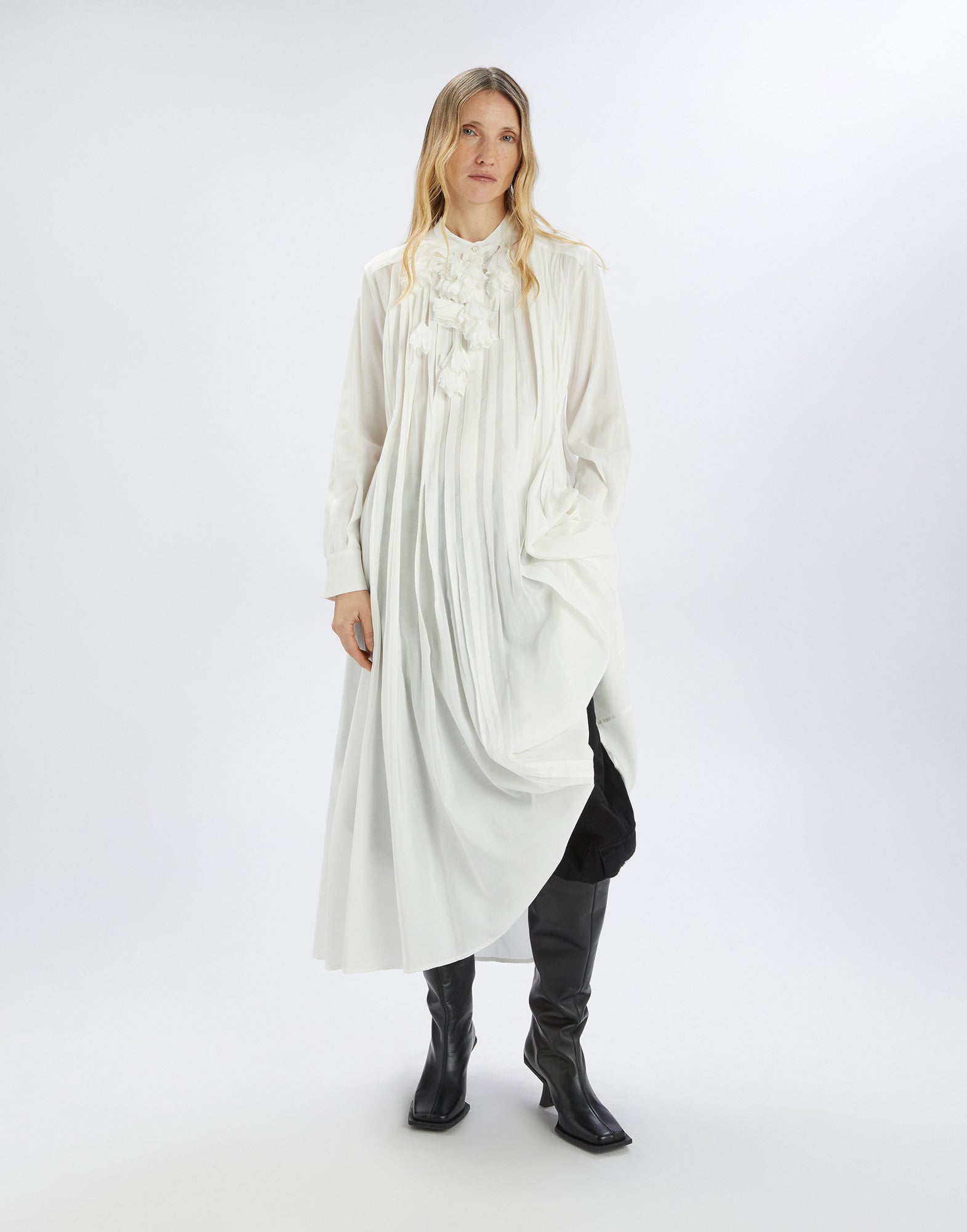 Frontalansicht einer Frau, die das weiße GALAXY Kleid trägt, mit Stehkragen, floraler Applikation am Kragen, langen Ärmeln und asymmetrischem Saum.