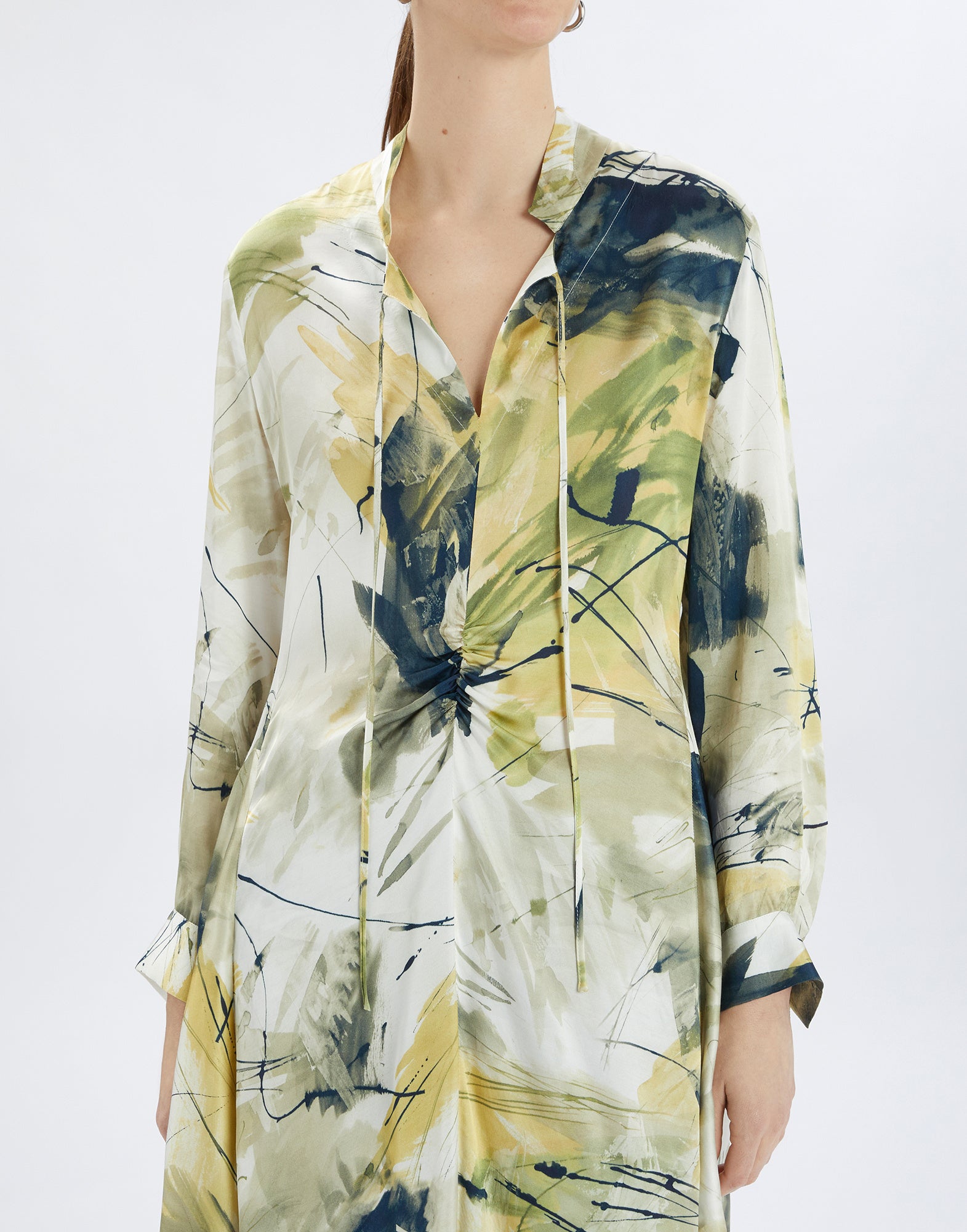 Frontalansicht: Person trägt das FILO Kleid mit abstraktem Druck in Gelb- und Grüntönen, Stehkragen, offenem V-Ausschnitt und langen Ärmeln.