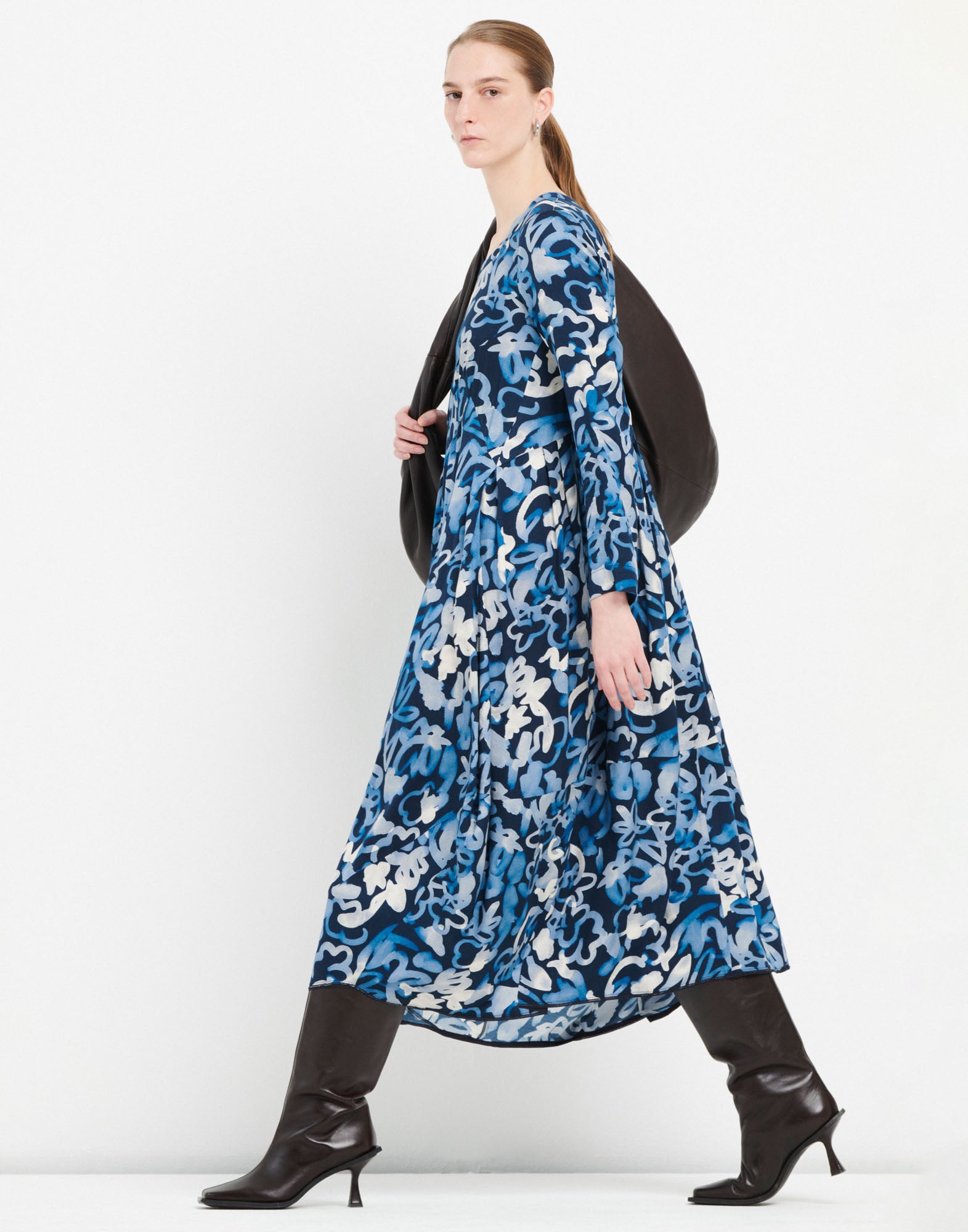 Seitenansicht einer Person im AWAKENING Kleid mit leuchtend blauem Muster, ballonartigem Rock und Dreiviertelärmeln, kombiniert mit schwarzen Stiefeln.