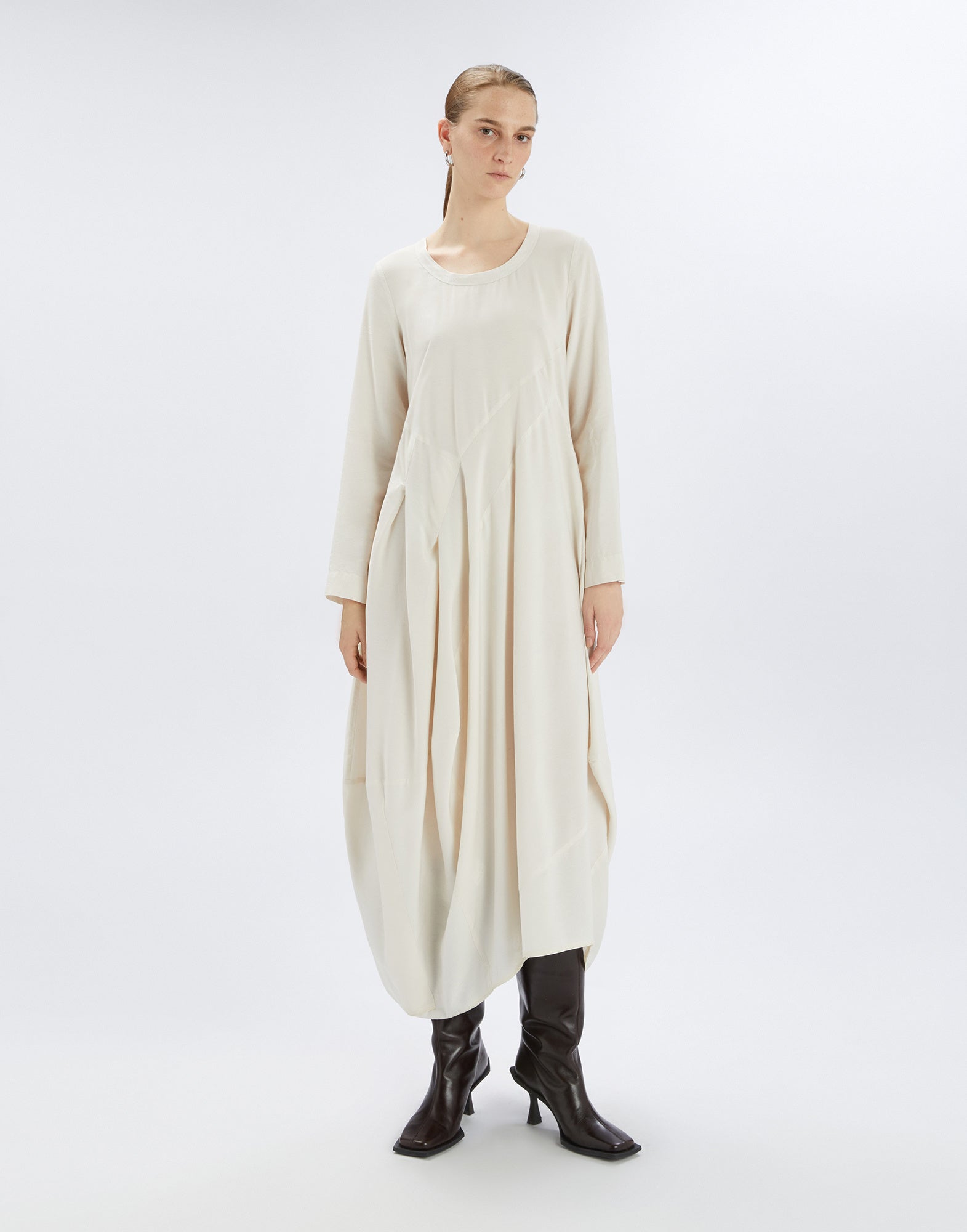 Frontalansicht: AWAKENING Kleid in hellem Farbton mit langem Ballonrock, langen Ärmeln, Rundhalsausschnitt und passendem Stoffgürtel, getragen von einer Frau.