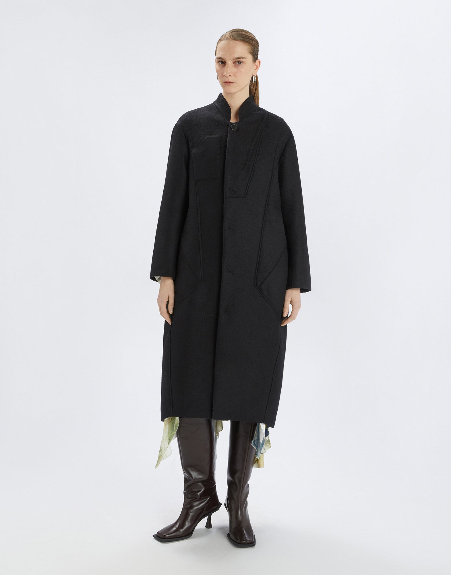 Frontalansicht: Eine Frau trägt den schwarzen PANTO Mantel mit Oversize-Passform, Stehkragen und sichtbaren Nähten. Der Mantel reicht bis zum Knöchel.