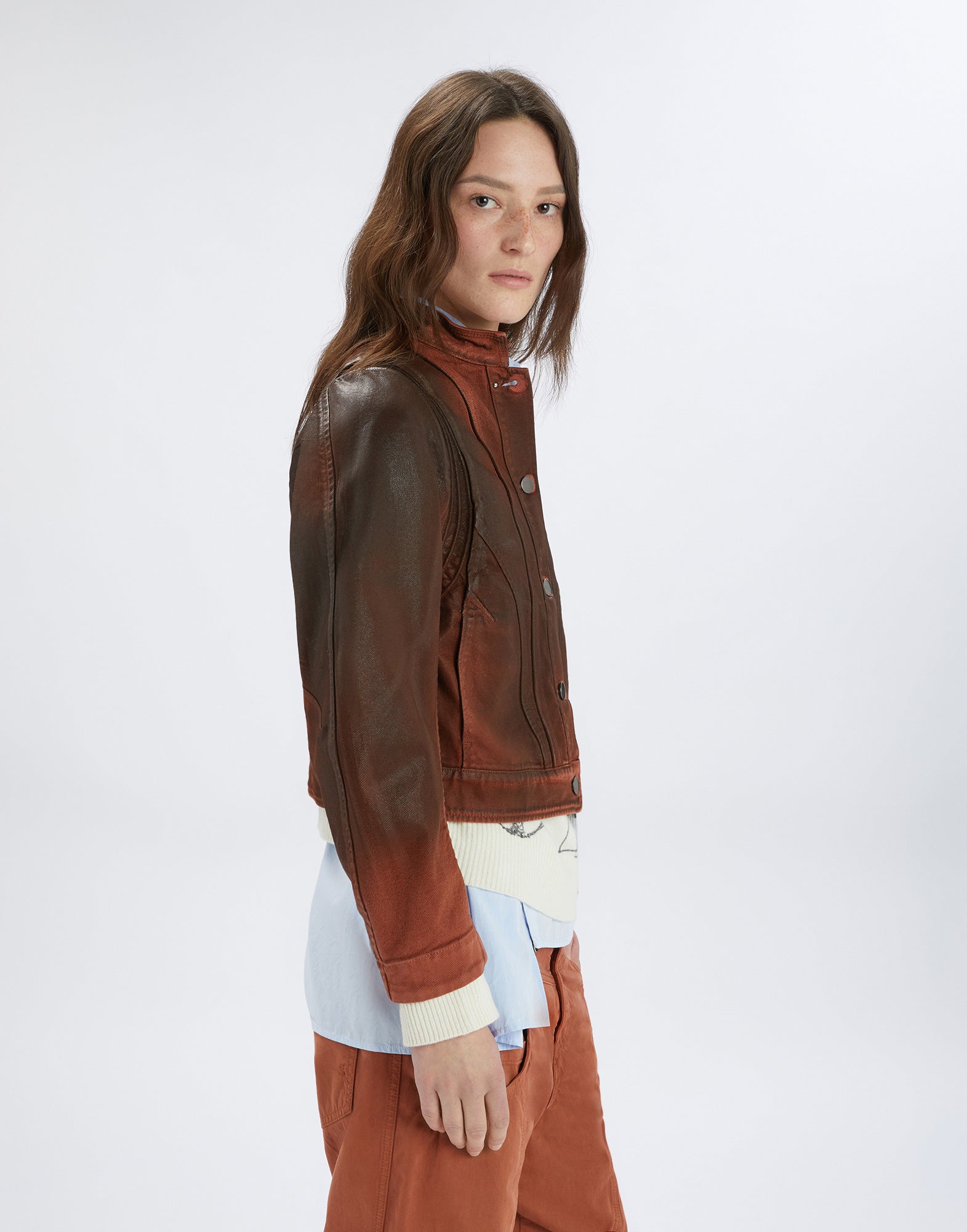 Seitenansicht einer Frau, die die TENDRIL-Jacke im Workwear-Stil trägt. Die Jacke hat einen Lederlook, sichtbare Steppnähte, einen Stehkragen und Metallknopfleiste.