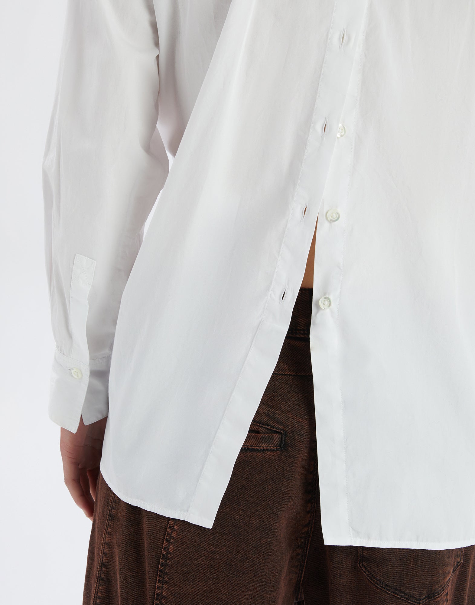 Detailansicht, seitlicher Blick auf das DEADLINE Hemd mit weißem, leichtem Baumwollstoff, sichtbarem hinterem Verschluss und asymmetrischem, abgerundetem Saum.