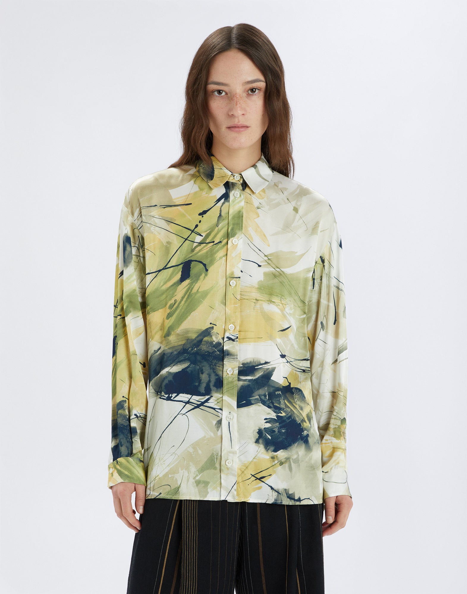 Front view: person wearing the KINFOLK shirt with abstract brushstroke pattern in yellow, green, and cream shades, featuring long sleeves and button placket.