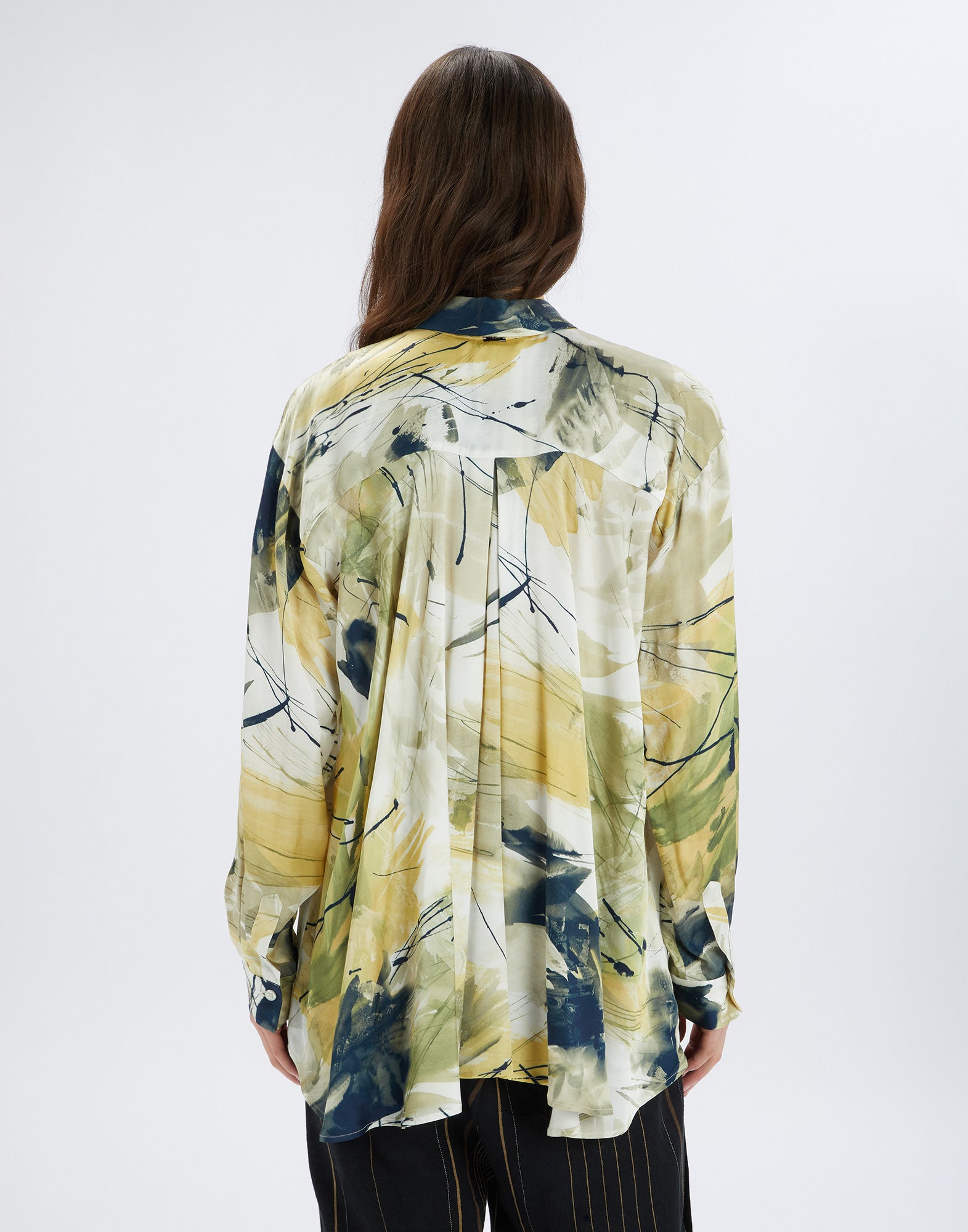 Back view of the KINFOLK shirt featuring an abstract print in yellow, green, and cream tones, turn-down collar, and long sleeves, worn by a person.