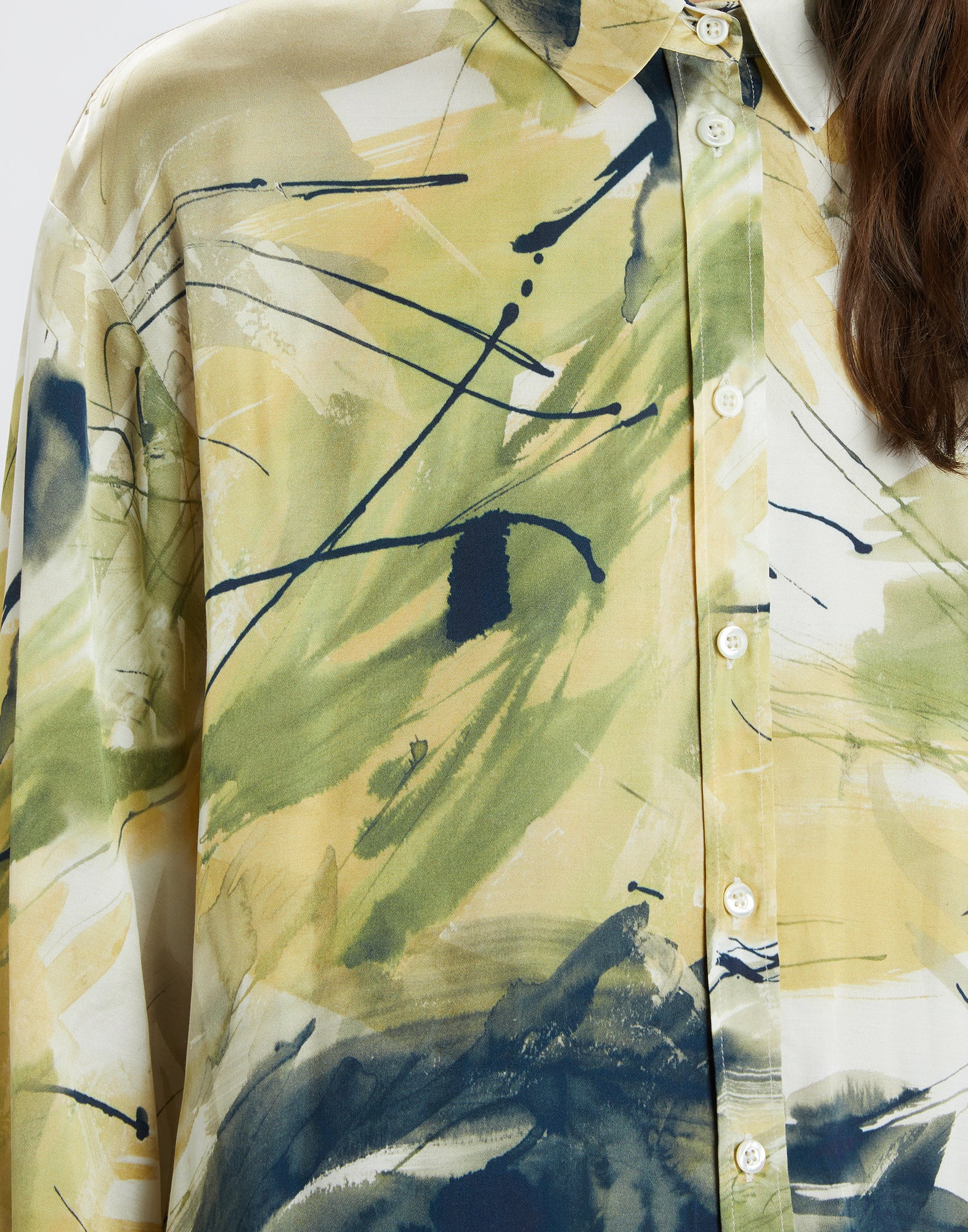 Detail view of the KINFOLK shirt with abstract, painterly pattern in yellow, green, and cream tones, front button placket and notched collar, made of lightweight viscose.