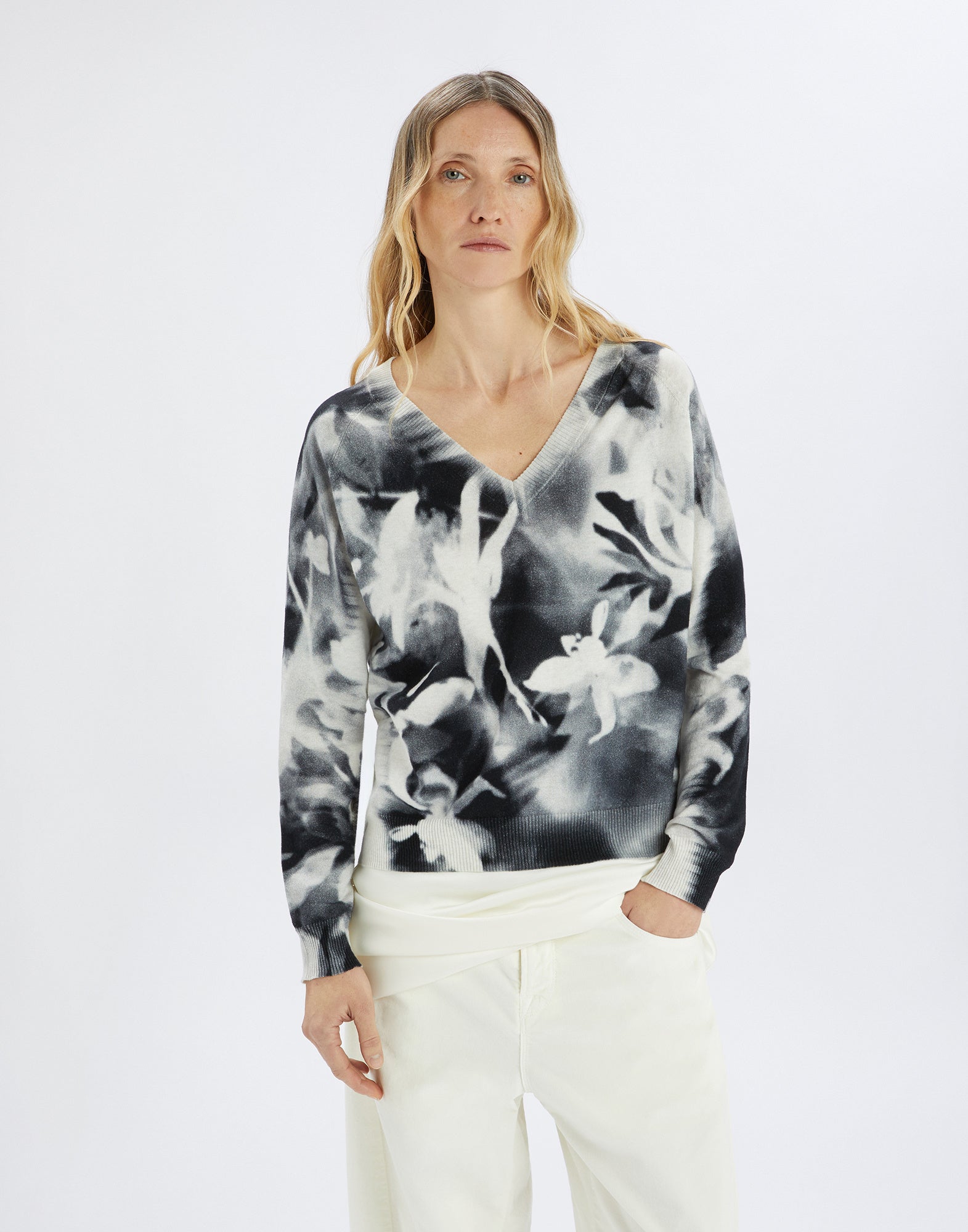 Front view: A woman wears the CECILIA top with floral black-and-white print, wide V-neckline, and relaxed fit, paired with light pants.