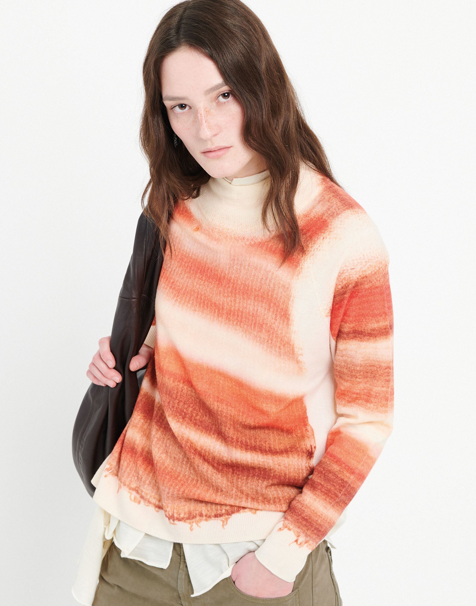 Frontalansicht: Person trägt RAMSEY Pullover aus feiner Merinowolle mit Streifenprint in Orangetönen auf cremefarbenem Grund, Stehkragen und Rippenbündchen.