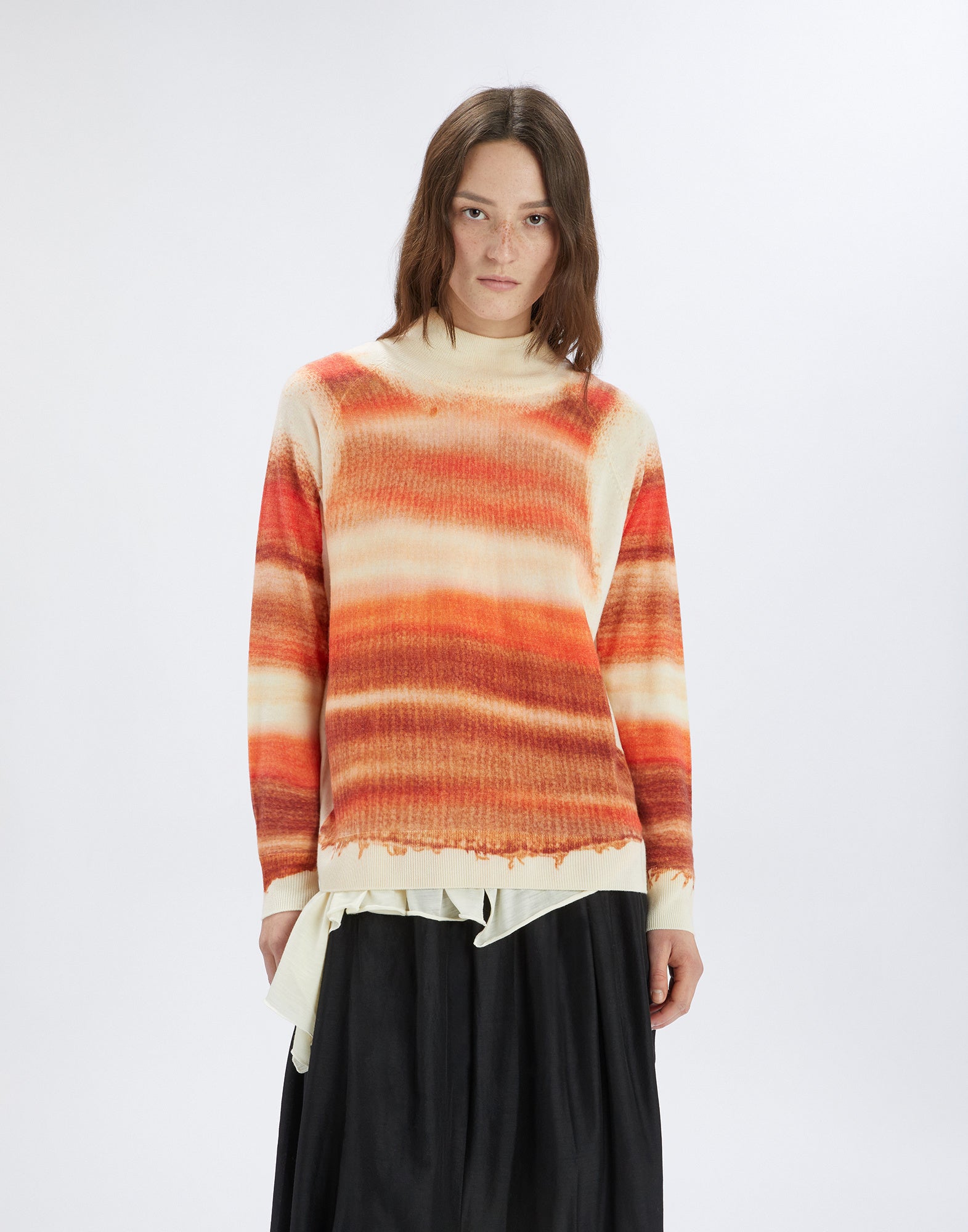 Front view: A woman wears the RAMSEY merino wool sweater with a cream base and orange-toned stripe print, stand collar, and ribbed cuffs.