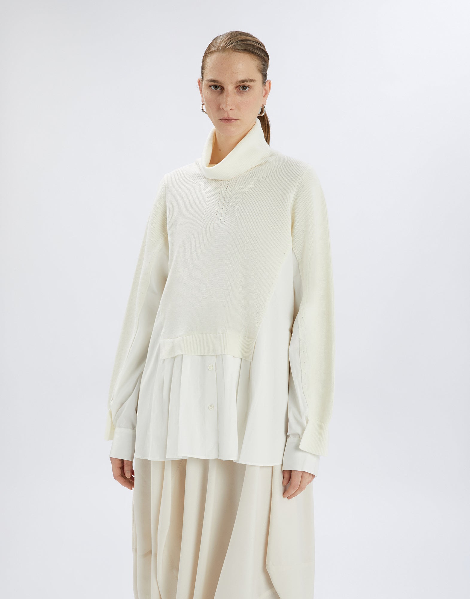 Front view: person wears the cream-white HEART-BIT sweater with high neck, knitted top, and attached poplin insert with button placket at the bottom.