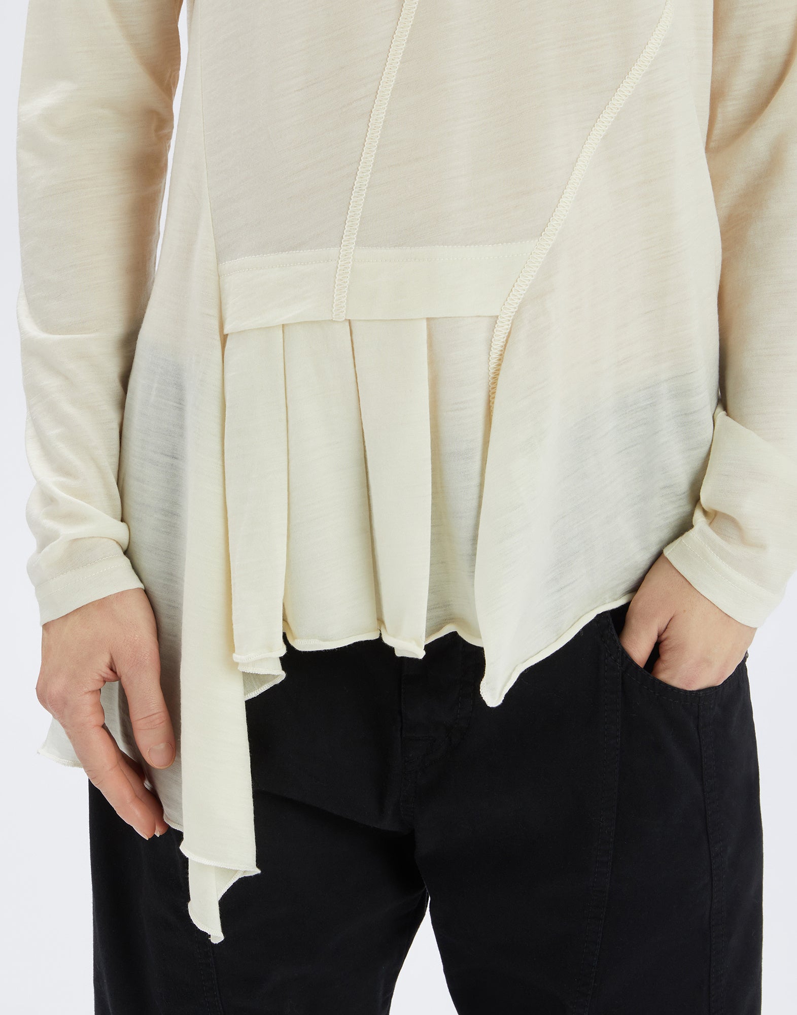 Detailansicht: Person trägt den hellen Pulli MATELOT aus ultraleichtem Woll-Jersey mit asymmetrischem Schnitt, seitlichem Jabot-Einsatz und unregelmäßigem Saum.