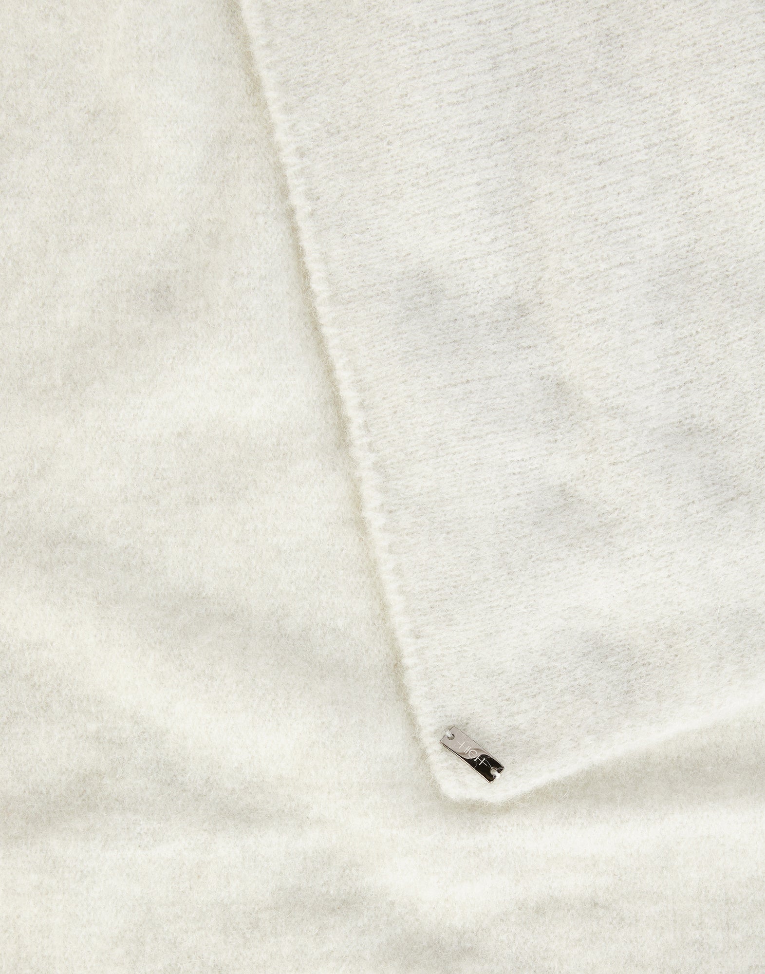 Detailansicht: FROSTY zeigt einen weichen, cremeweißen Stretch-Alpakawollschal mit feiner Struktur und kleinem Metall-Label an einer Ecke.