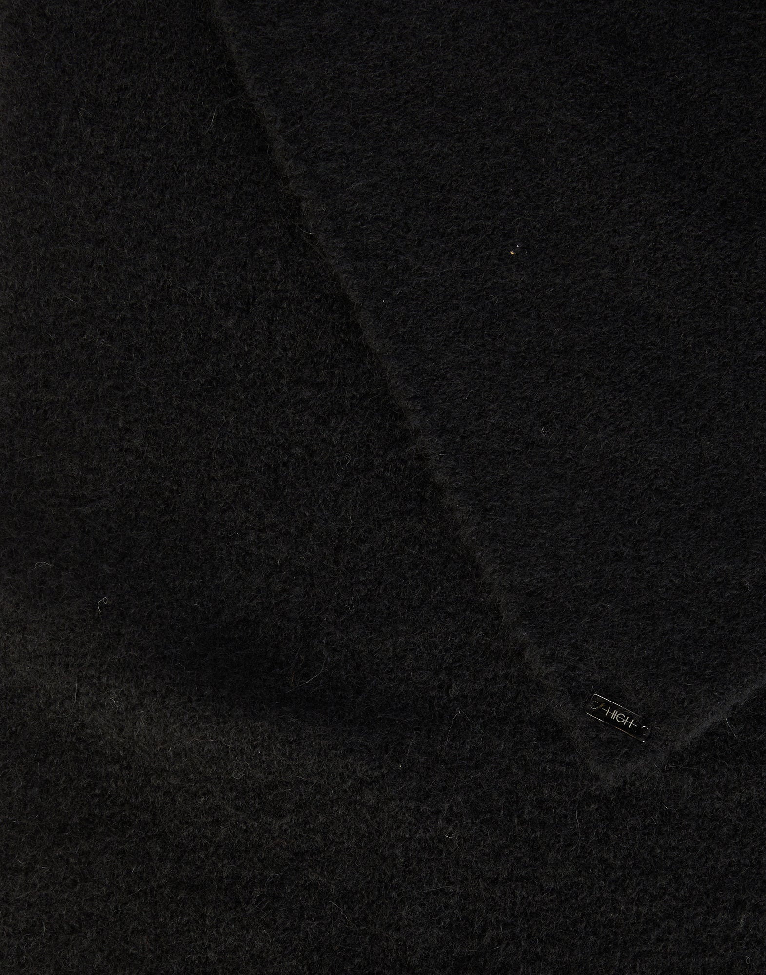 Detailansicht des FROSTY Stretch-Alpakawollschals in Schwarz, weiche, flauschige Textur, sichtbares kleines Etikett unten rechts, Materialstruktur deutlich erkennbar.