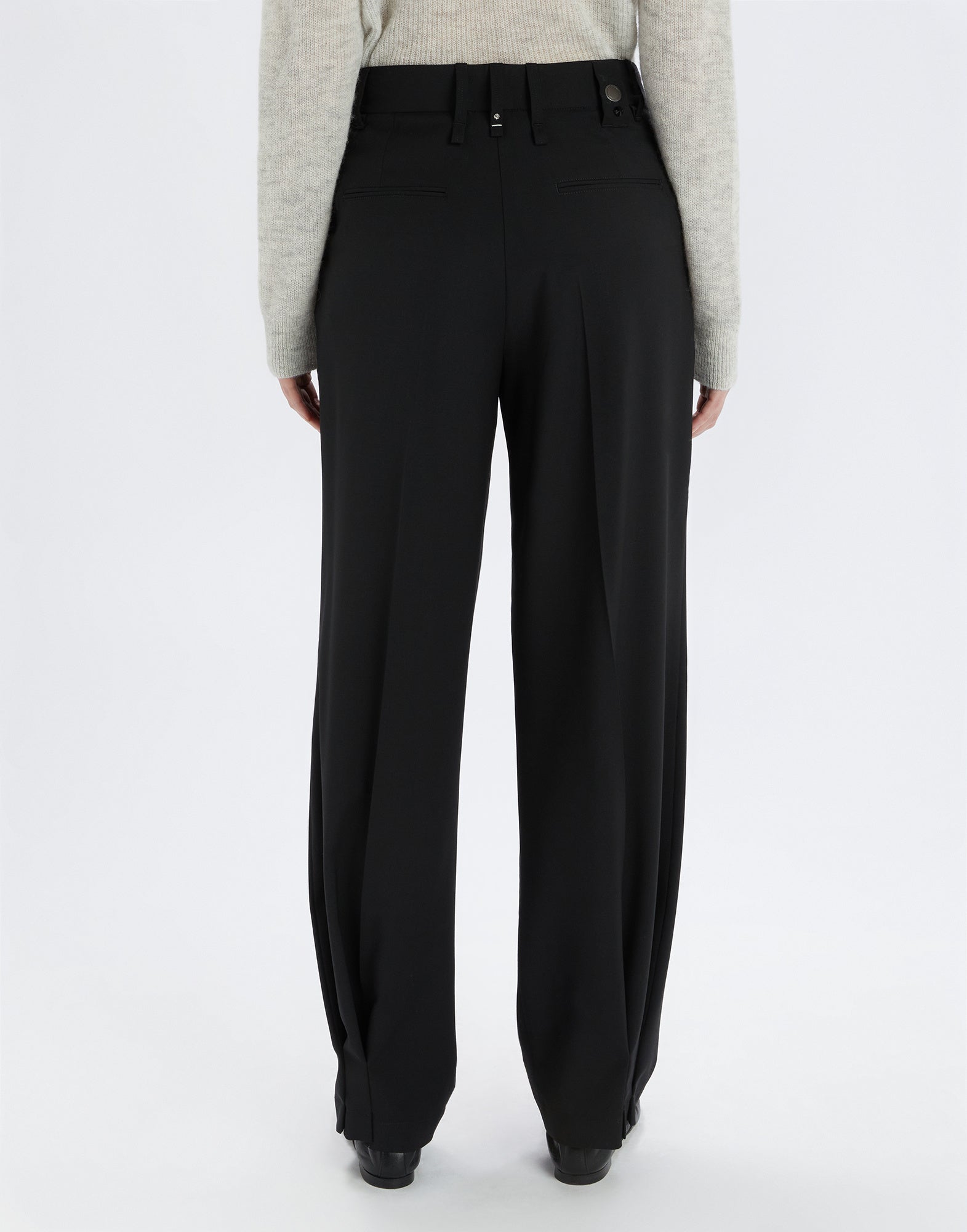 Rear view of a person wearing the RELY black pants; relaxed fit, welted back pockets, and extra-fine wool material visible.