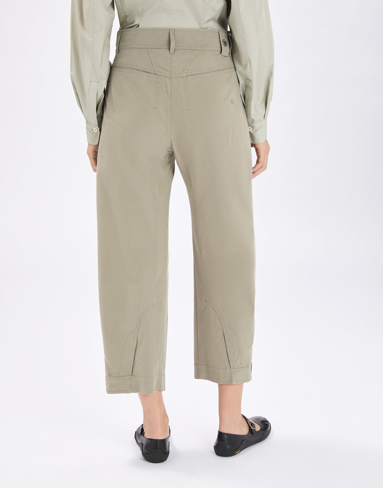 Rear view: Model wears the beige wide-leg LOLA pants with high waist, visible seams, inverted pocket details and belt-loop style tabs at the hem, paired with a light green blouse.