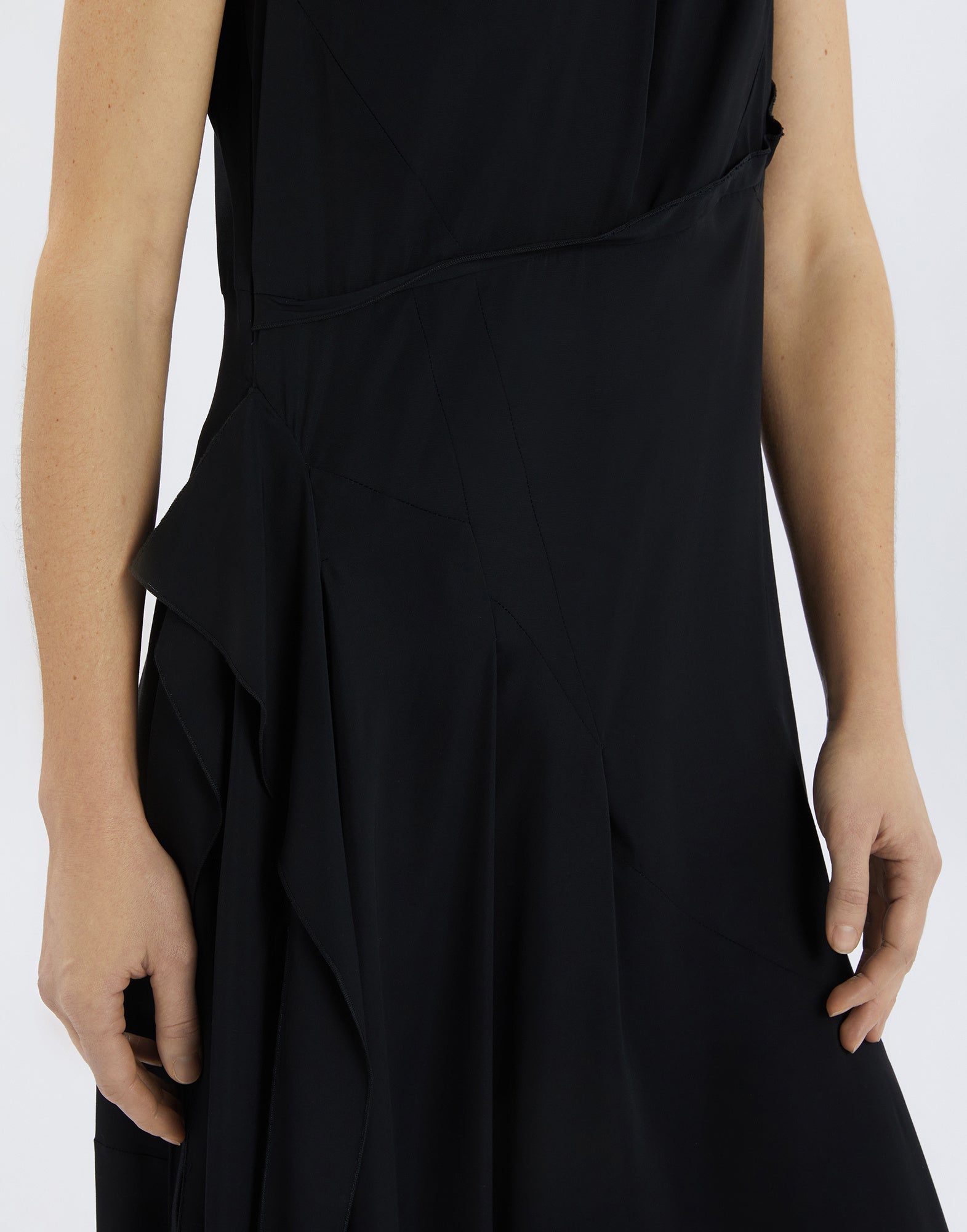 Detail view of the SOUND OFF dress displays a side area with flowing black fabric, draping, and subtle seam lines, focusing on the hip and waist.