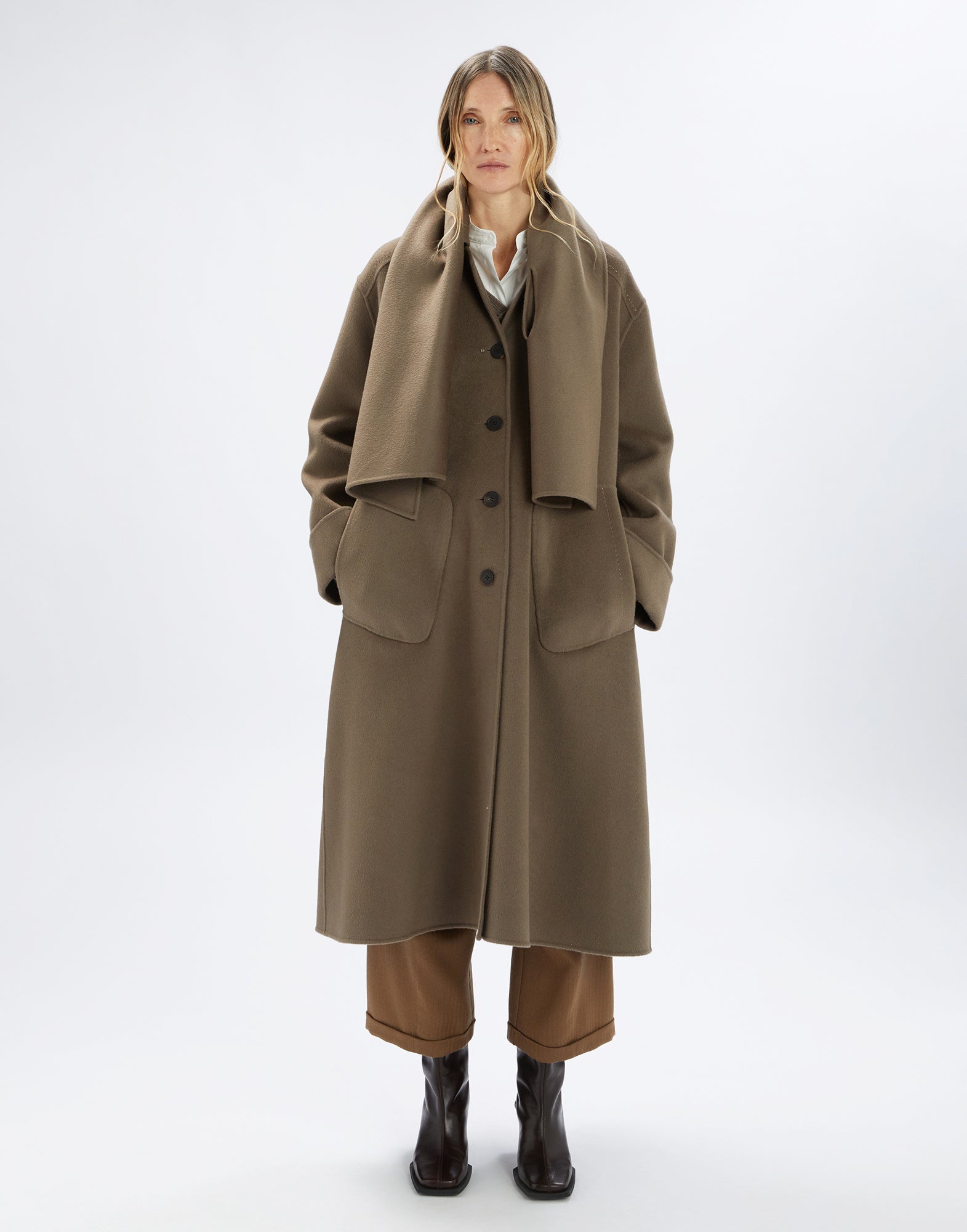 Front view: Person wears the SPIRE coat in khaki with a clean, slightly oversized silhouette, attached scarf, notched collar, and large welt pockets.