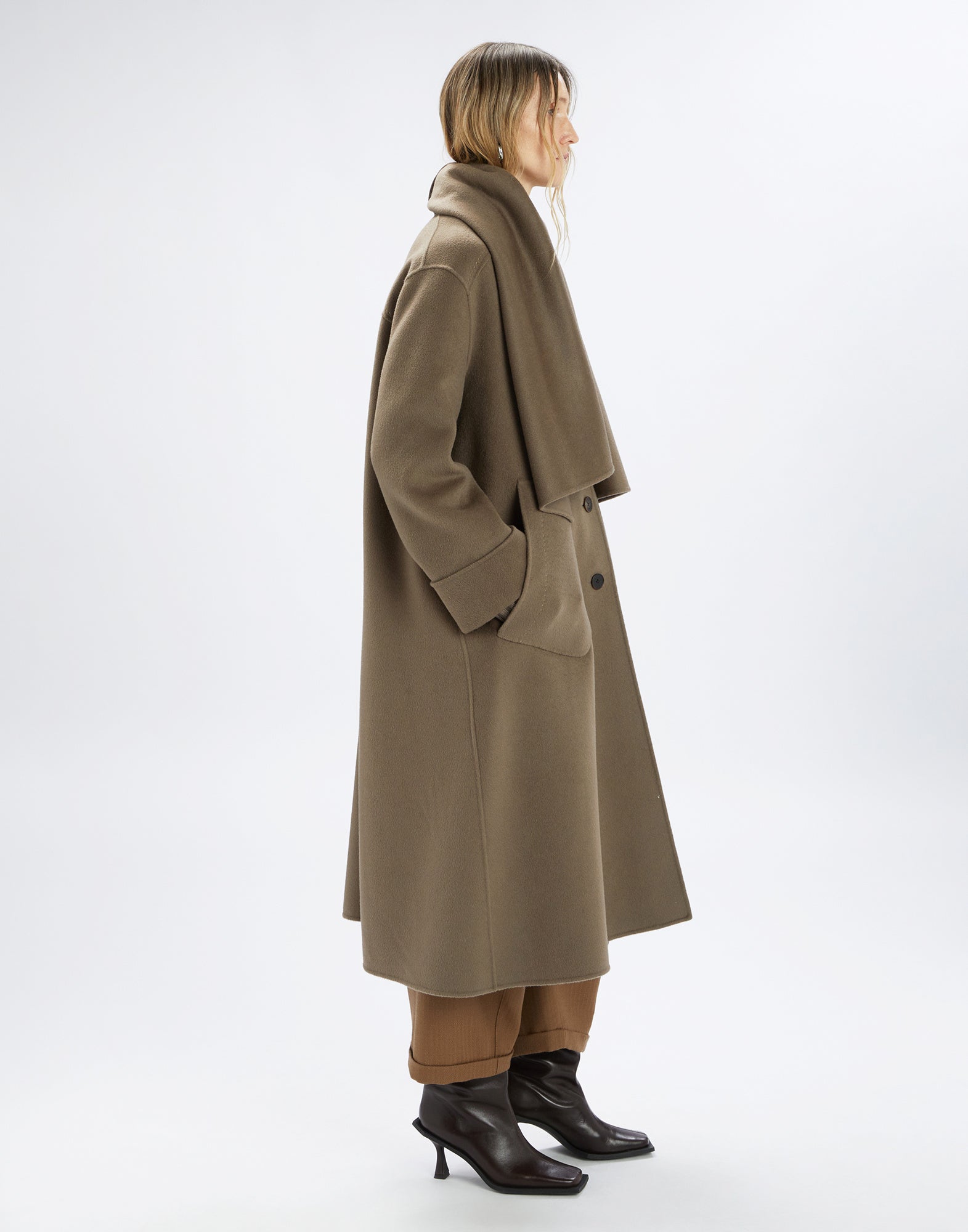 Side view of a person wearing the elegant SPIRE coat. The double cashmere coat features an oversized cut, large welt pockets, removable scarf, and visible topstitching.