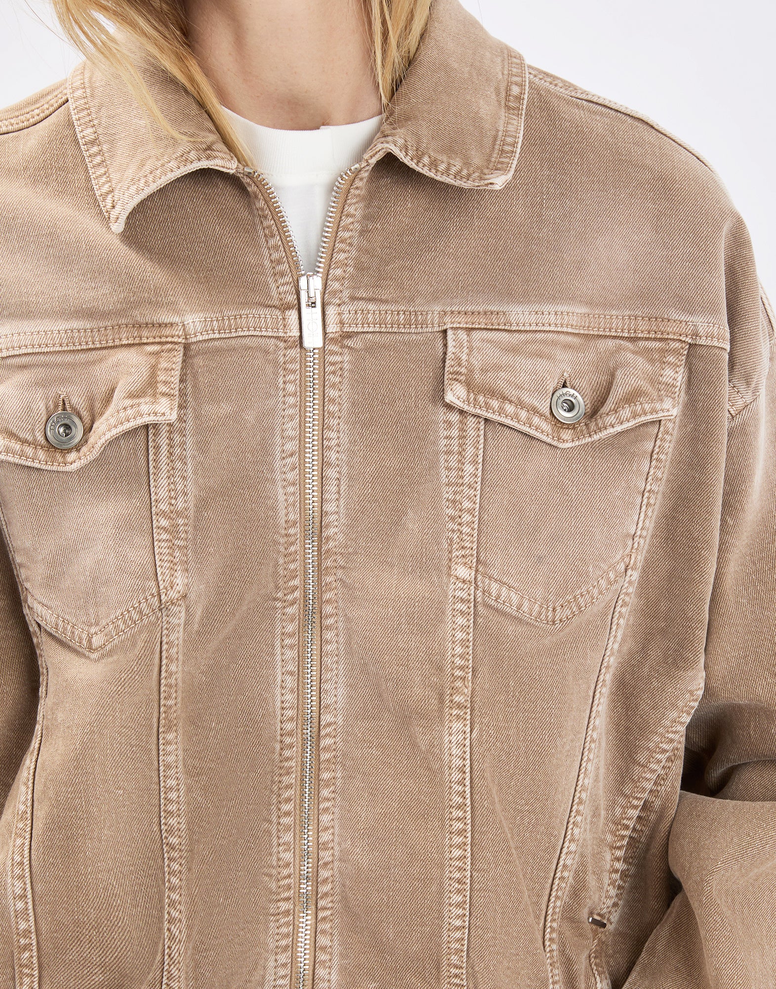 Detailansicht, Frontalansicht: Person trägt die beige Denim-Bomberjacke COMPACT mit Metallreißverschluss, umgeschlagenem Kragen, Pattentaschen mit Knöpfen auf der Brust und leicht verwaschener Optik.