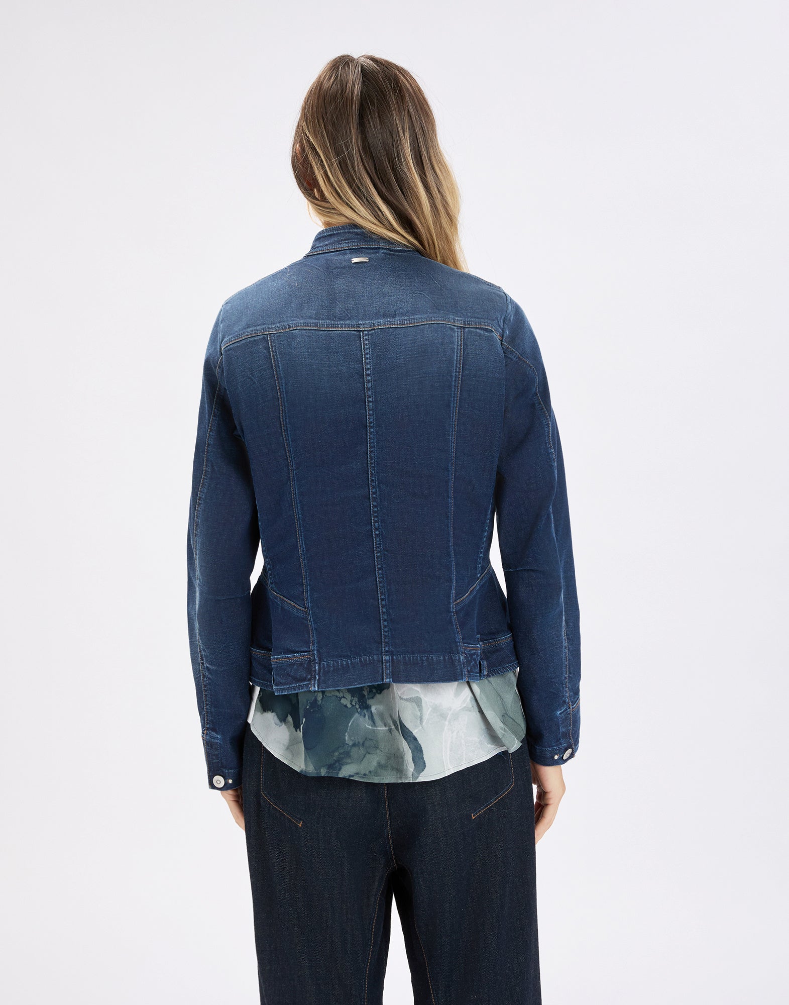 Back view: person wearing the slim-fit AHOY denim jacket in dark blue, with visible vertical seams, high stand collar and waist-defining cut over a patterned blouse.