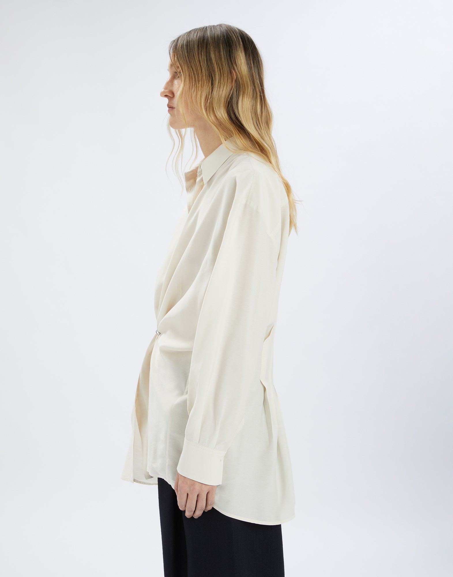 Seitenansicht einer Person, die die cremefarbene SKYLARK Bluse trägt; lockerer Schnitt, umgelegter Kragen, lange Ärmel und D-Ring Detail vorne sichtbar.