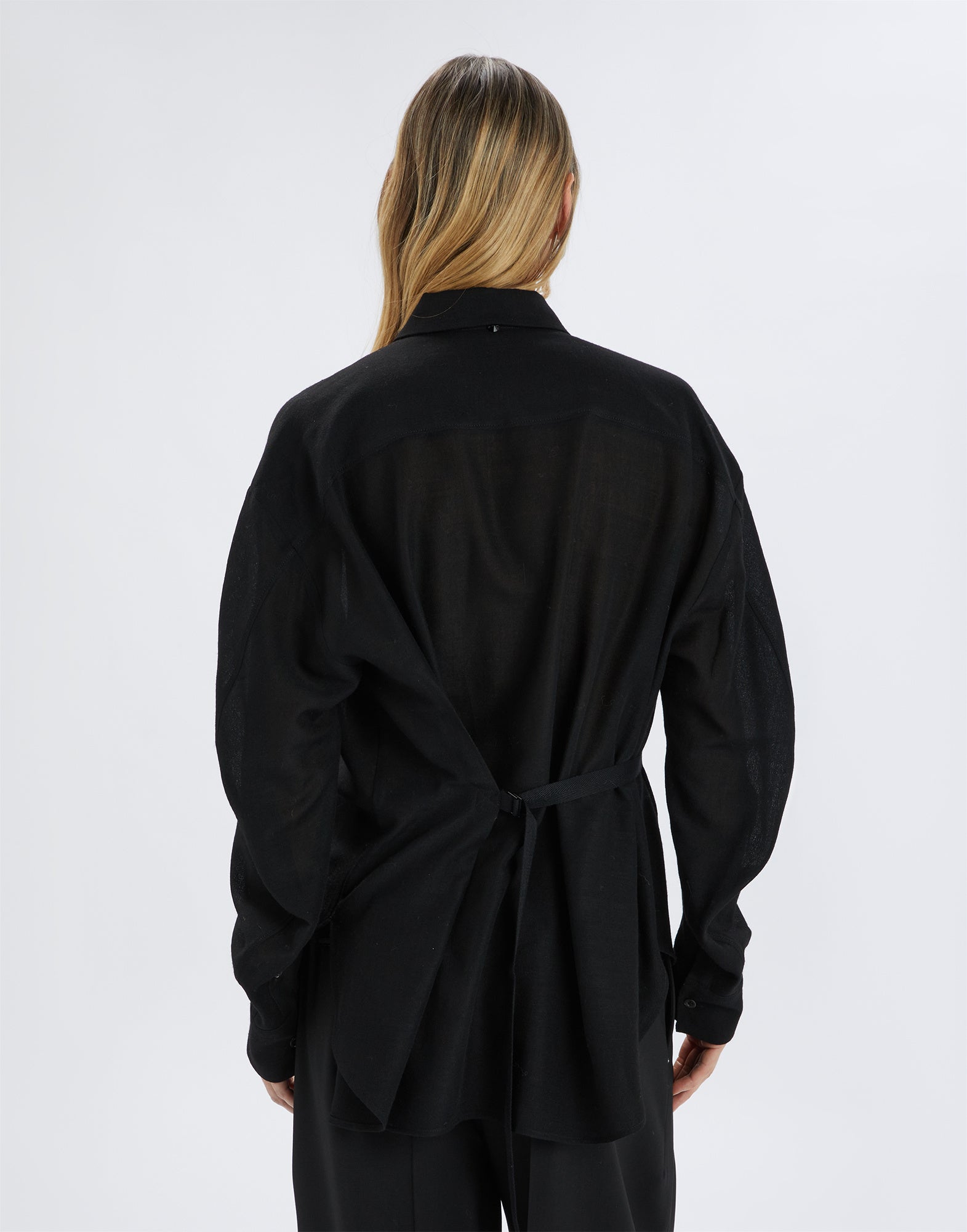 Back view of a person wearing the black SCOOT blouse made from extra-fine, sheer wool gauze. Visible: D-ring on the back for adjustable fit.