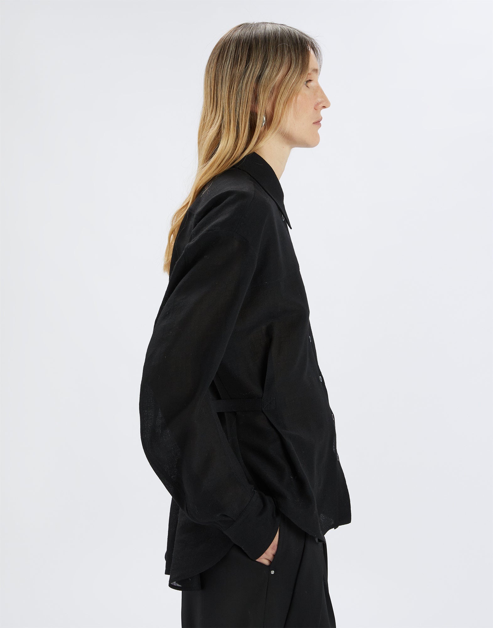 Side view of the SCOOT blouse in extra-fine black wool gauze on model, featuring puff sleeves, notched collar, and back D-ring for adjustable fit.