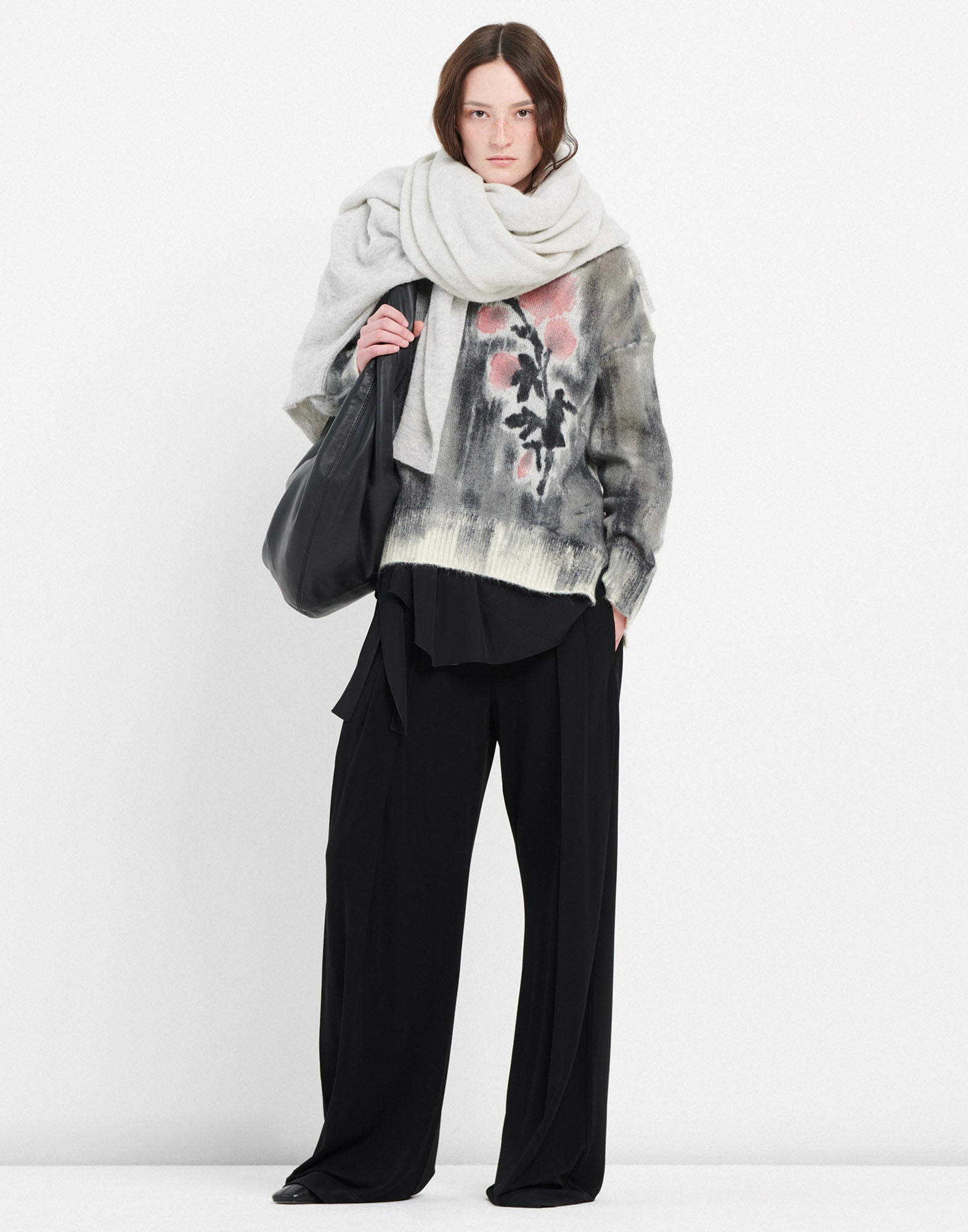 Frontalansicht: Person trägt den Pullover NEUTRON mit boxy Schnitt, Farbverlauf und rosa Blumenmotiv auf der linken Seite, dazu schwarze Hose und hellen Schal.