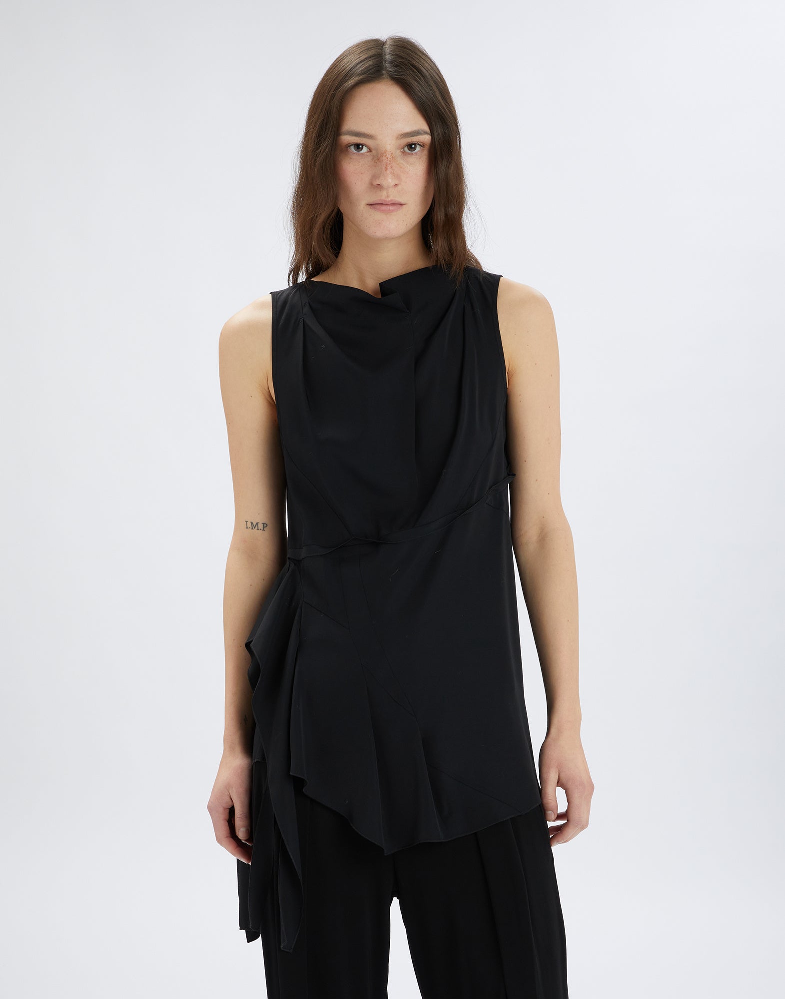 Front view of the sleeveless TIMBRELL top in black, featuring a square neckline, romantic side ruffle, and asymmetric hem, worn by model.