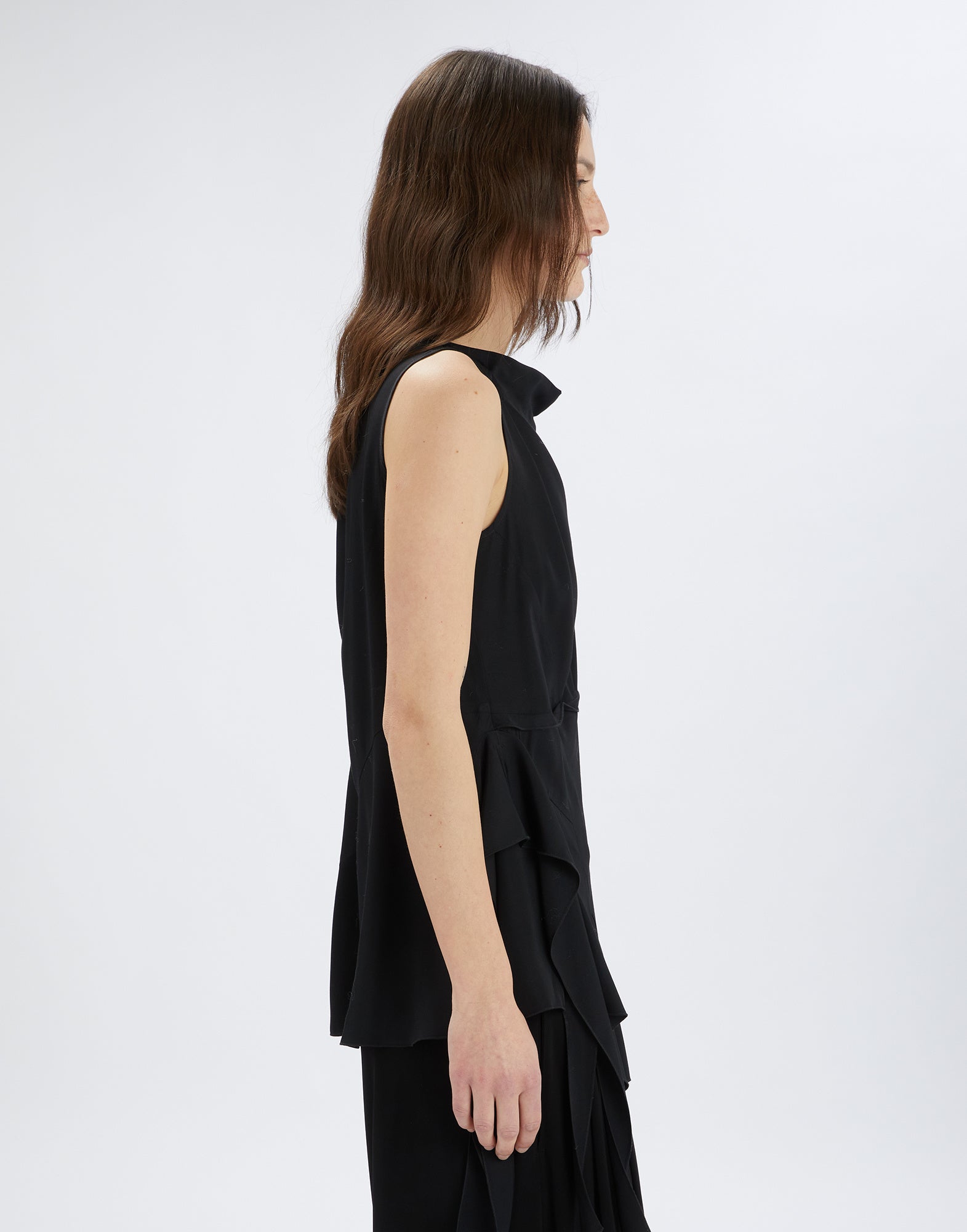 Side view of the TIMBRELL top, sleeveless, with square neckline, asymmetric hem, and romantic side ruffle, in flowing black viscose.