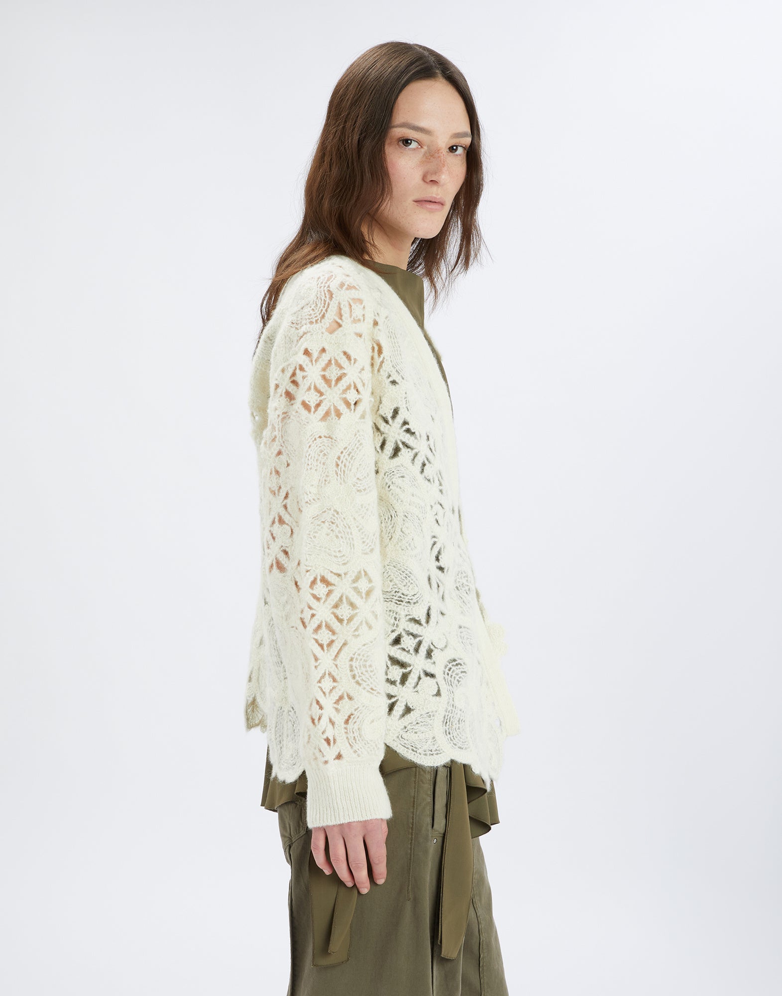 Side view of a model wearing the BOHEME cardigan. Light floral openwork embroidery, long sleeves, asymmetric hem, and soft knit.