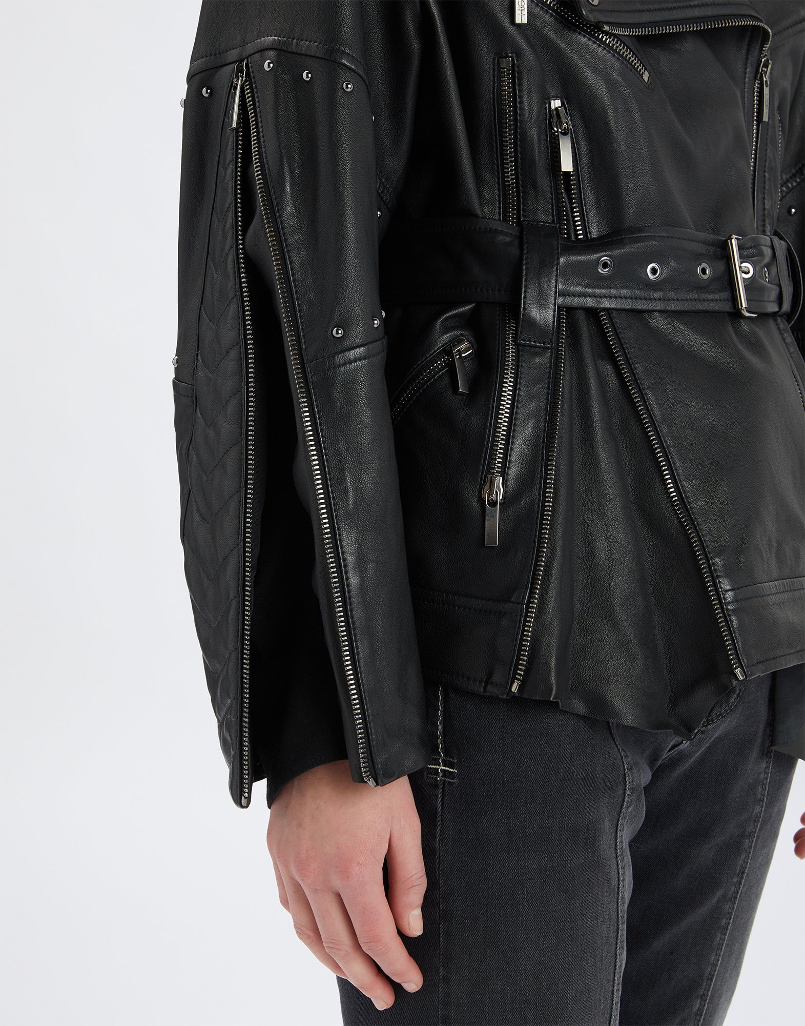 Side view detail of the TOMMY jacket, featuring black leather and shearling surface with visible zippers, micro studs, and a metal-buckle belt.
