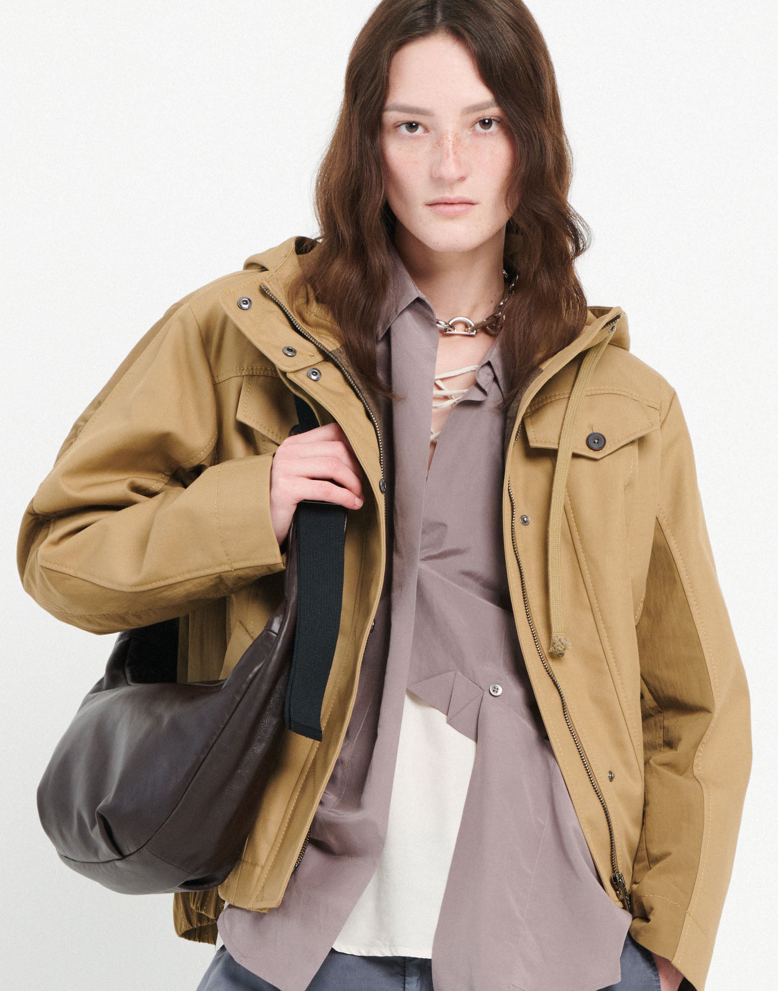 Front view: woman wears the ADMIRAL crossbody bag casually over the shoulder, bag made of dark leather with wide fabric strap, removable round wallet visible.