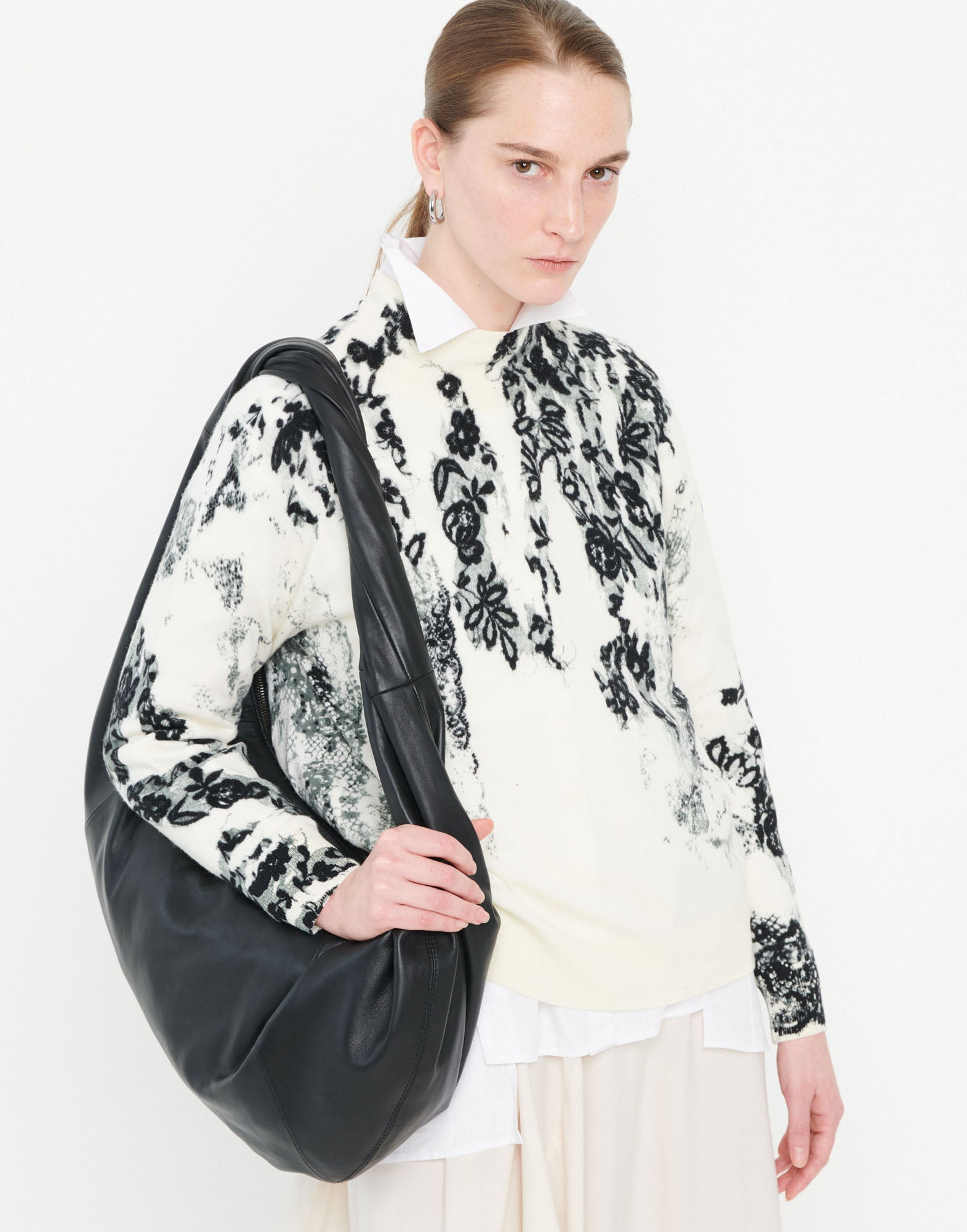 Front view of a person casually carrying the large REFLEX hobo bag in soft black nappa leather with braided handle over the shoulder.