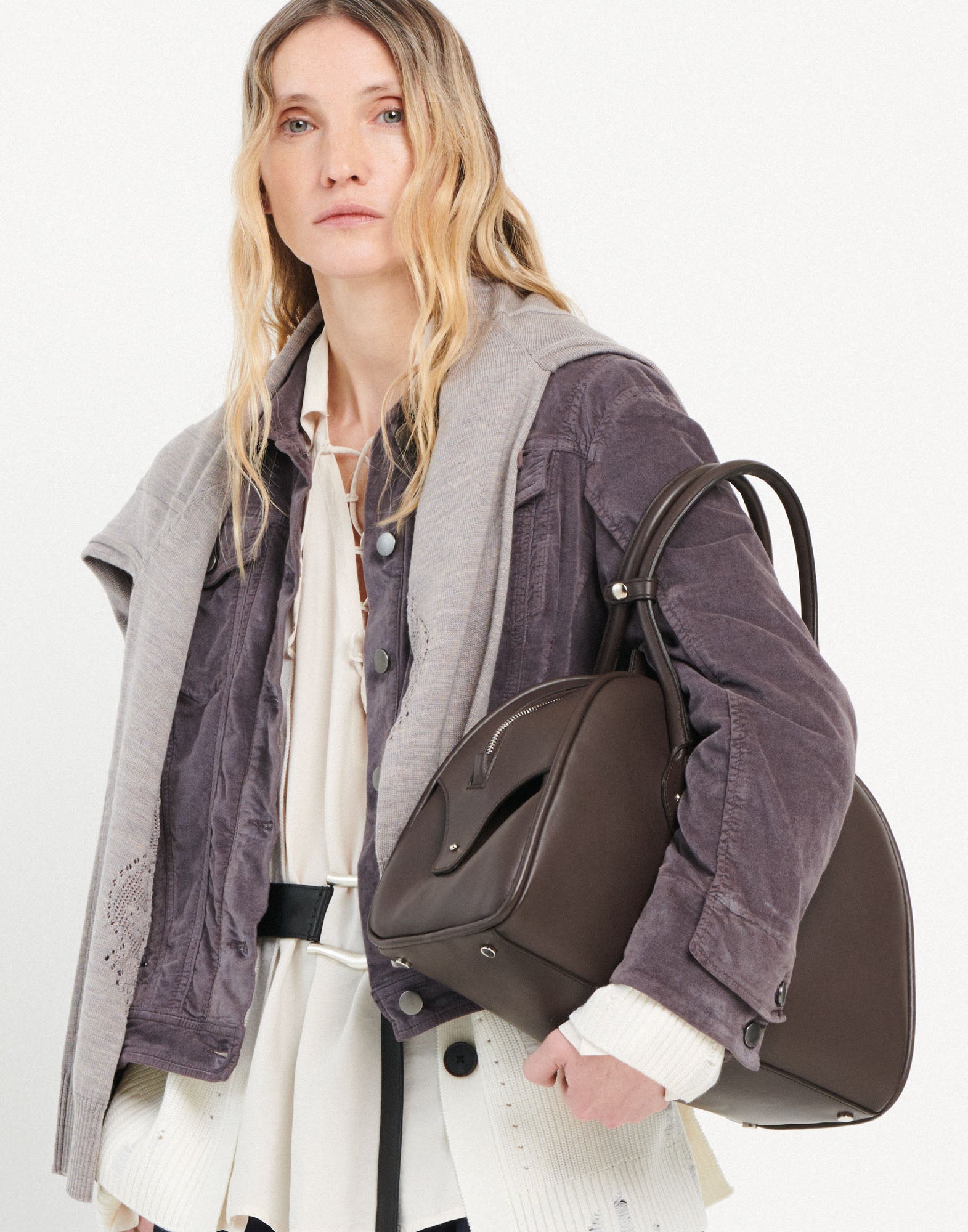 Front view: woman carries the BELUGA bag in brown calf leather with reinforced handles and decorative leather tag on her shoulder, modern design.