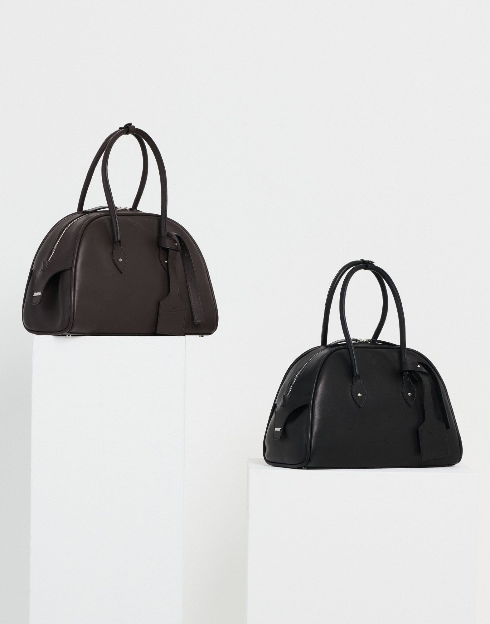 Front view of the BELUGA bag, modern bowling bag in brown and black with reinforced handles, double-slider zip, and decorative leather tag.