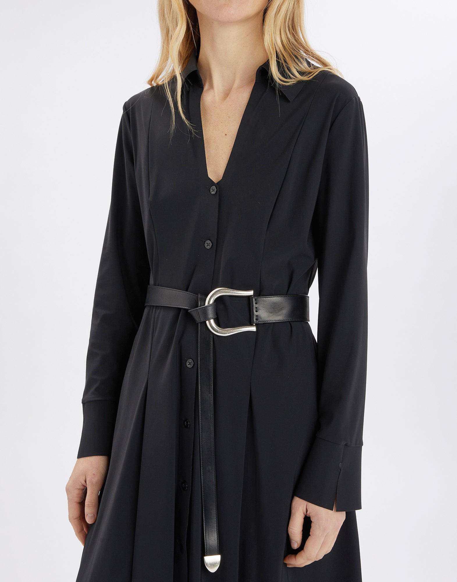 Frontalansicht einer Frau, die den SHORTY Gürtel aus schwarzem Kalbsleder mit großer antiksilberner Metallschnalle über einem schwarzen Kleid trägt.
