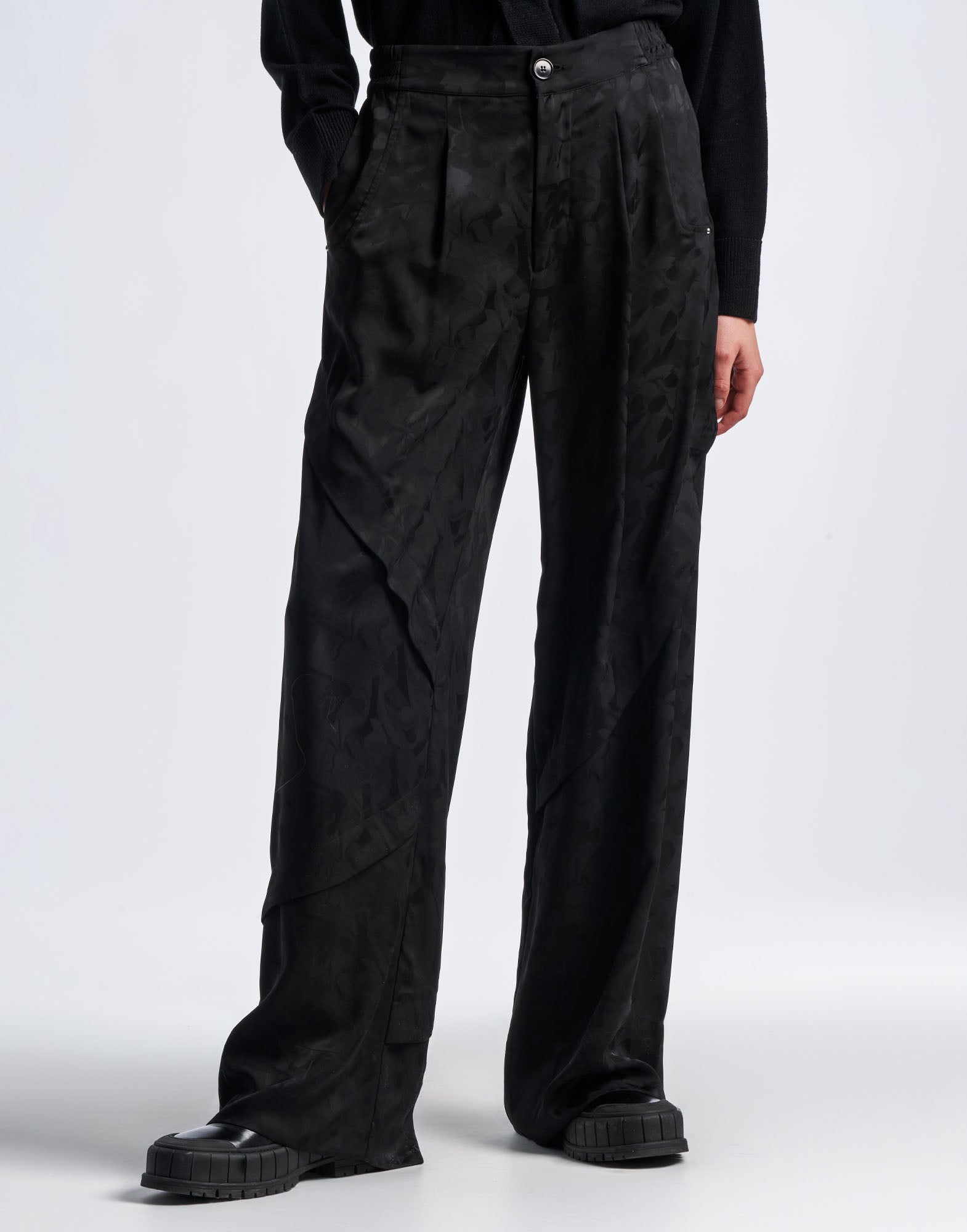 Frontalansicht der BORDERLINE Hose mit weitem Bein aus schwarzem Funktionssatin, Damast-Blumenmuster, silbernem Knopf, seitlichen Taschen und betontem, breitem Saum.