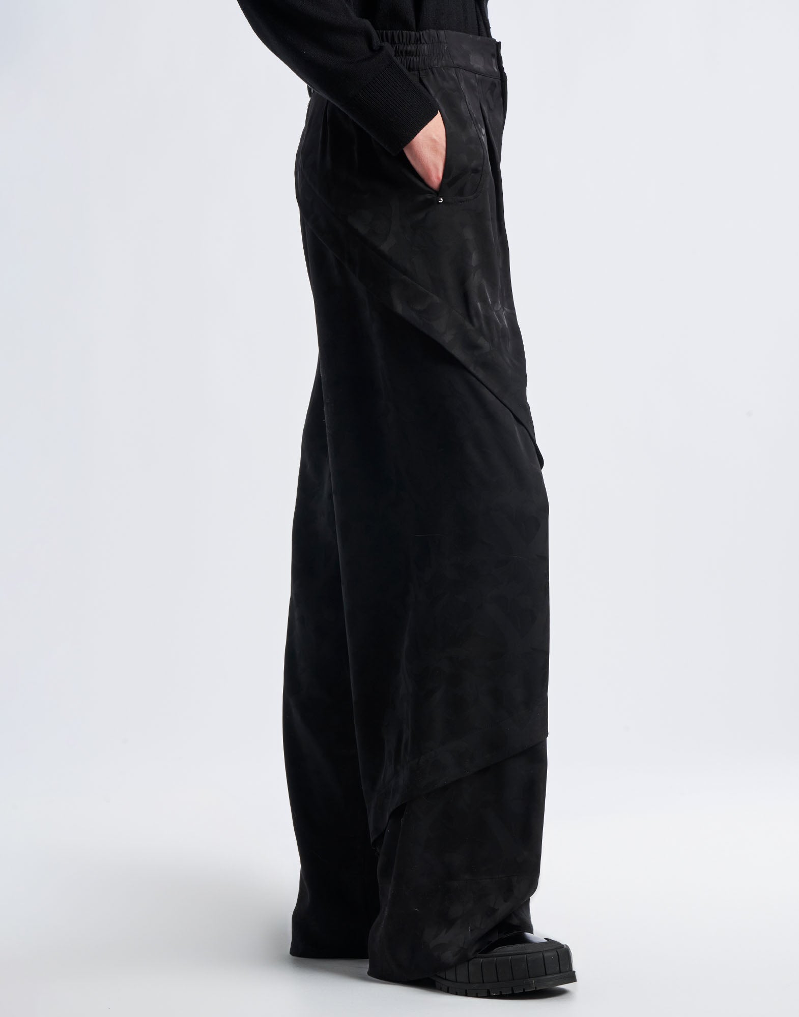 Seitenansicht der BORDERLINE Hose mit weitem Bein aus schwarzem Funktionssatin, sichtbaren diagonalen Nähten und eingesetzt elastischem Bund, getragen von einer Person.