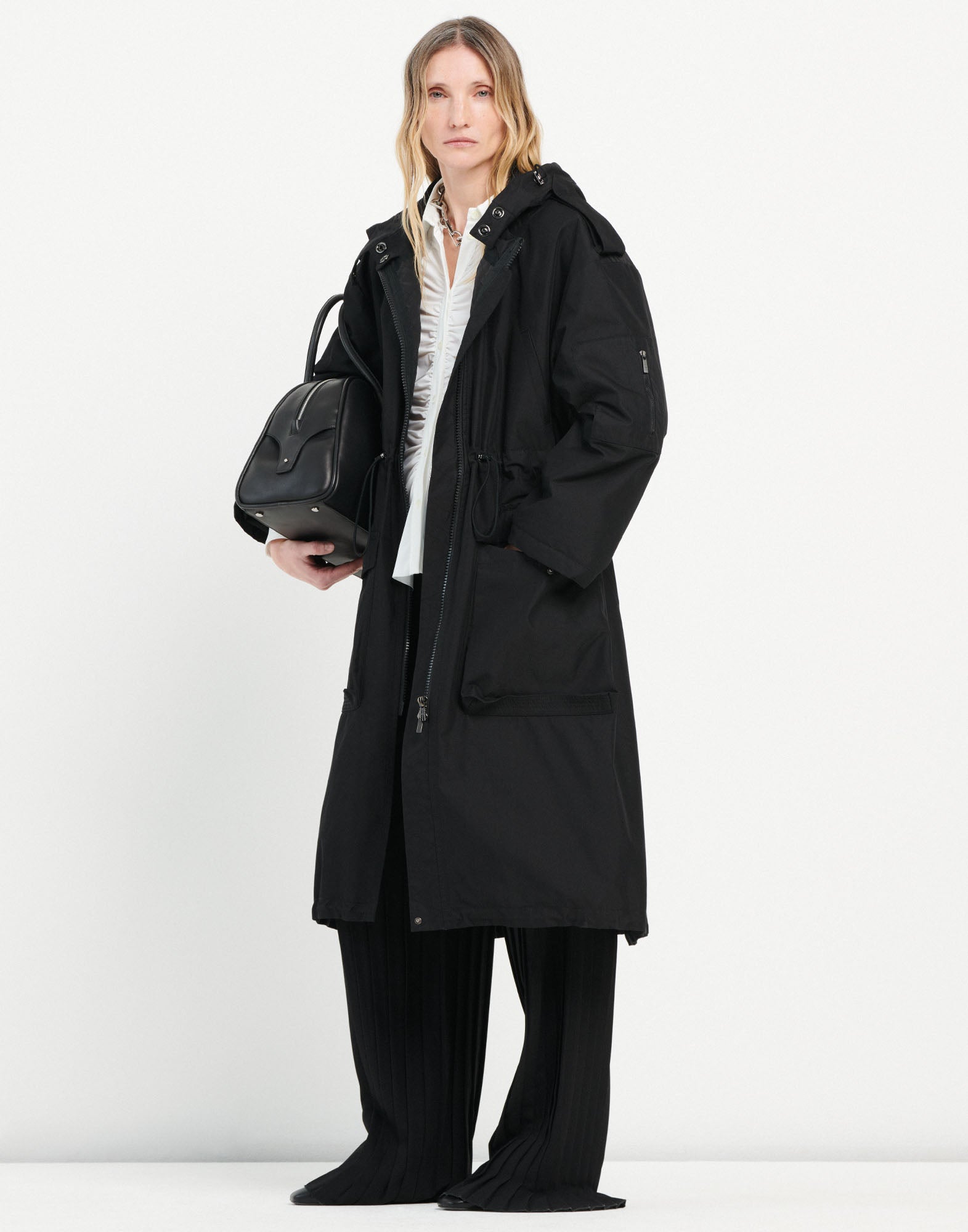 Front view of a woman wearing the DREW black palazzo trousers. The trousers feature straight, wide legs with prominent pleats reminiscent of classical columns.