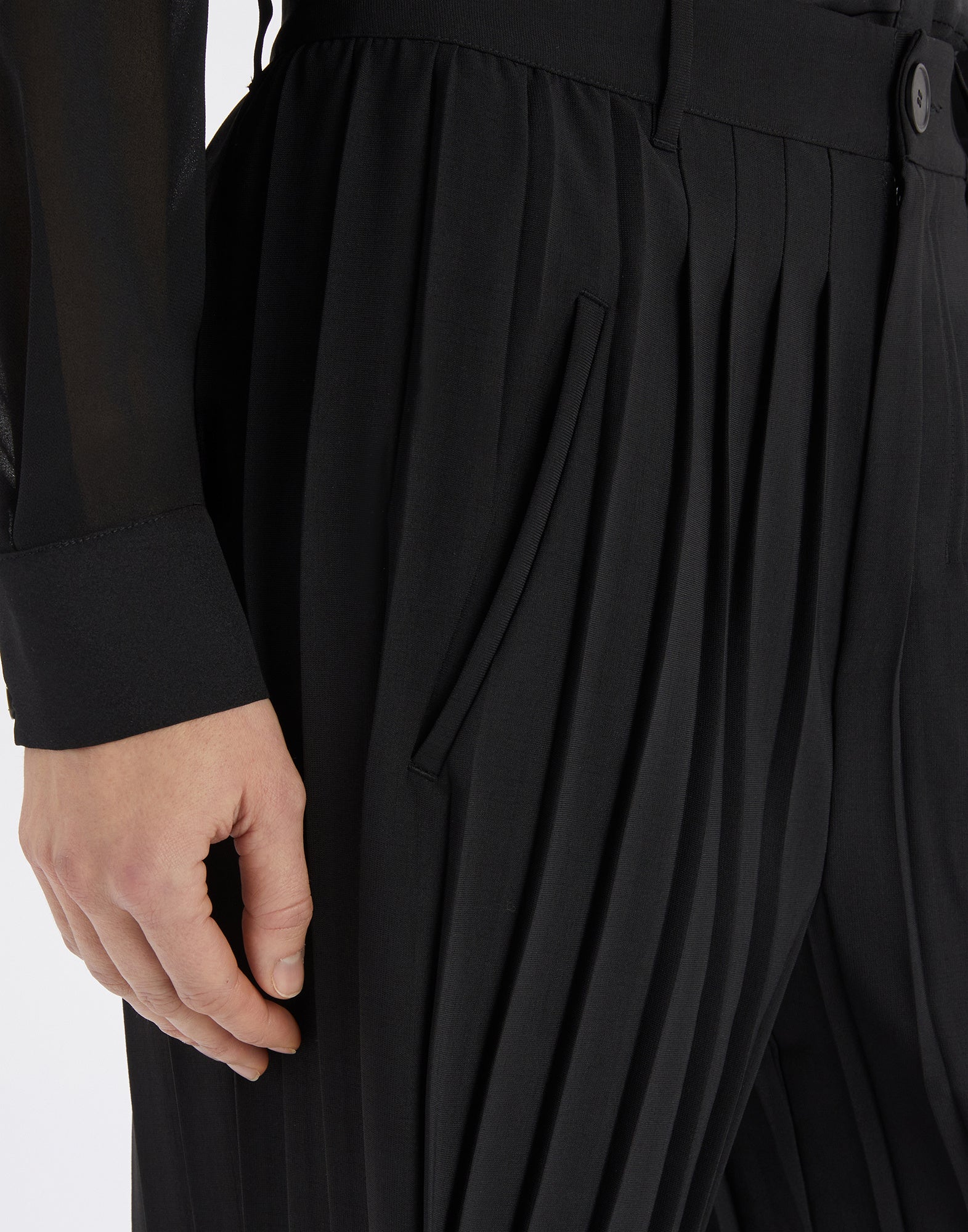 Side detail view: DREW palazzo trousers display fine Greco-Roman style pleats, waistband with belt loops, button closure, and diagonally set front pocket.