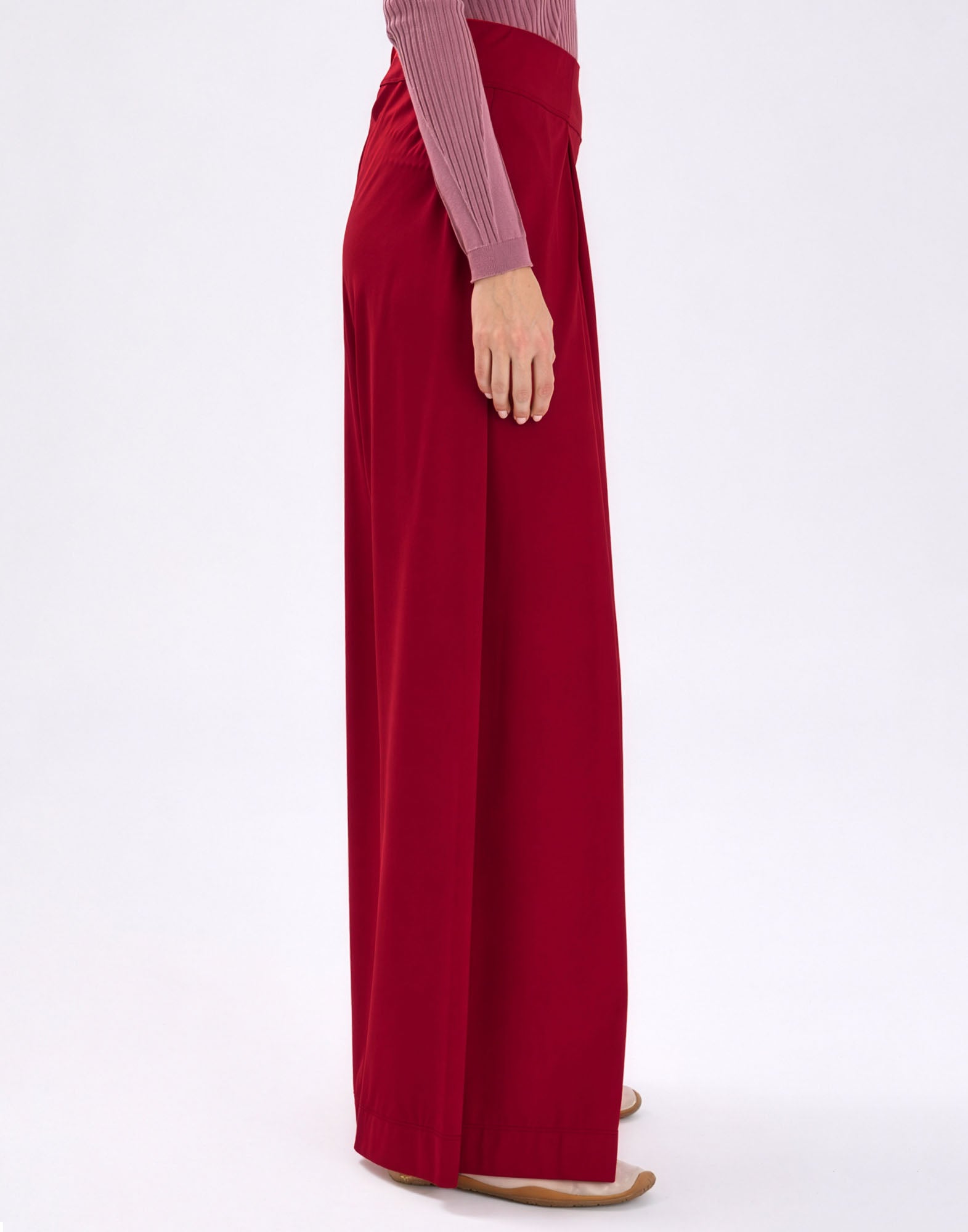 Side view: model wearing the wide-cut, floor-length DIMINISH pants in vibrant red with loosely draping legs, higher waist, and flowing, smooth Sensitive(R) fabric.