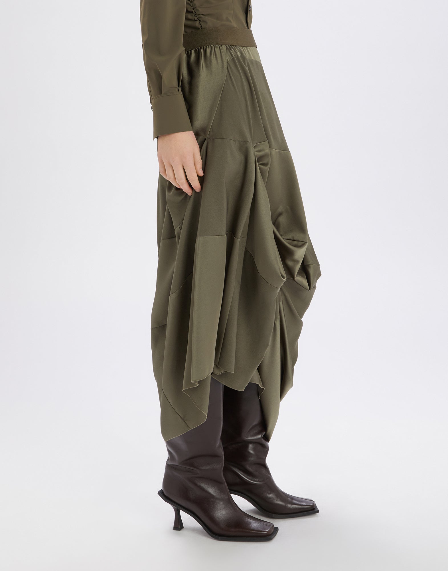 Seitenansicht einer Person, die den GEEK Rock in olivgrünem, fließendem Tech-Satin mit asymmetrischem, drapiertem Saum und elastischem Bund trägt.