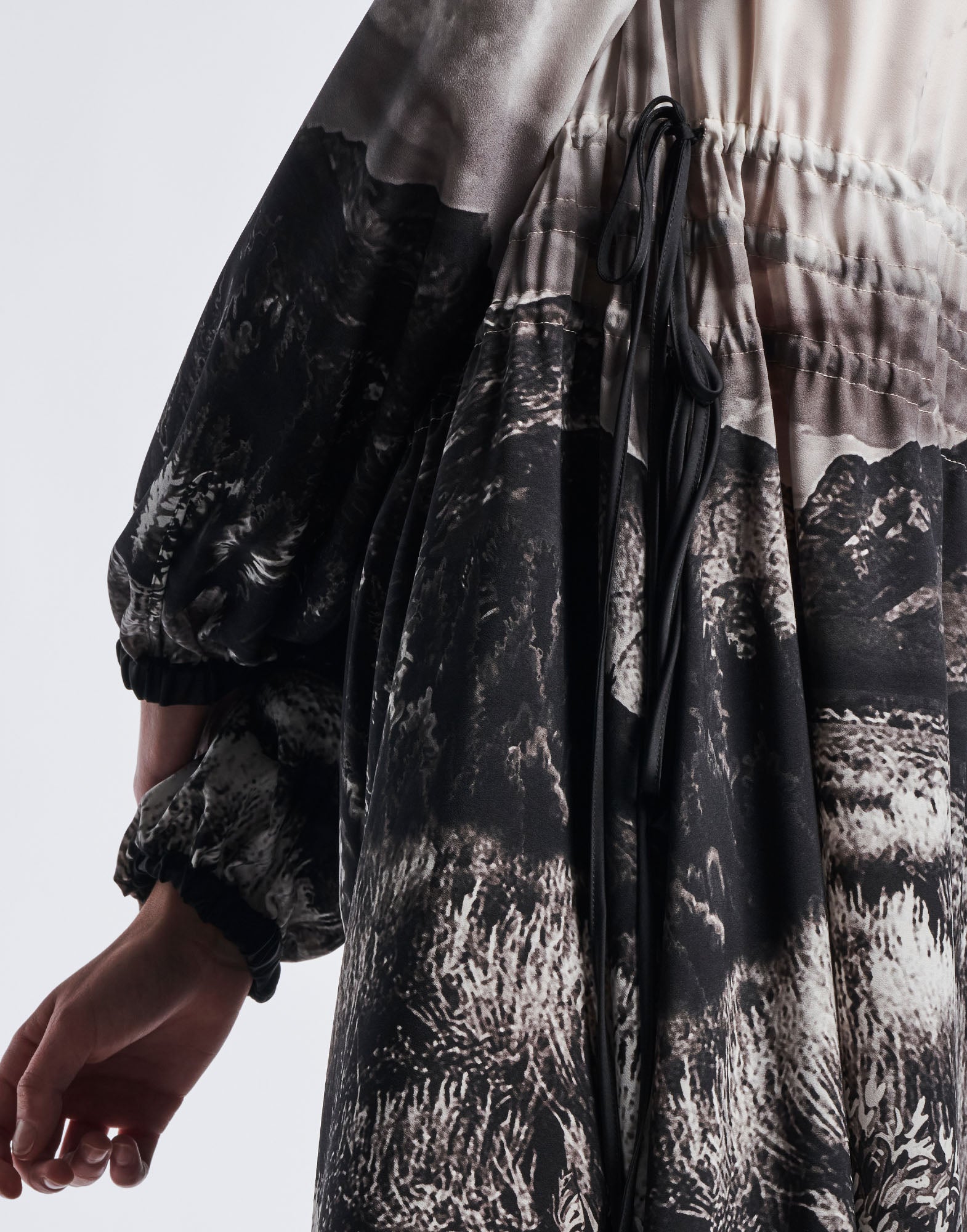 Detailansicht schräg des RHYMING Maxi-Kleids mit schwarz-weißem Landschaftsdruck, elastischen Glockenärmeln und seitlichem Kordelzug in der Taille.