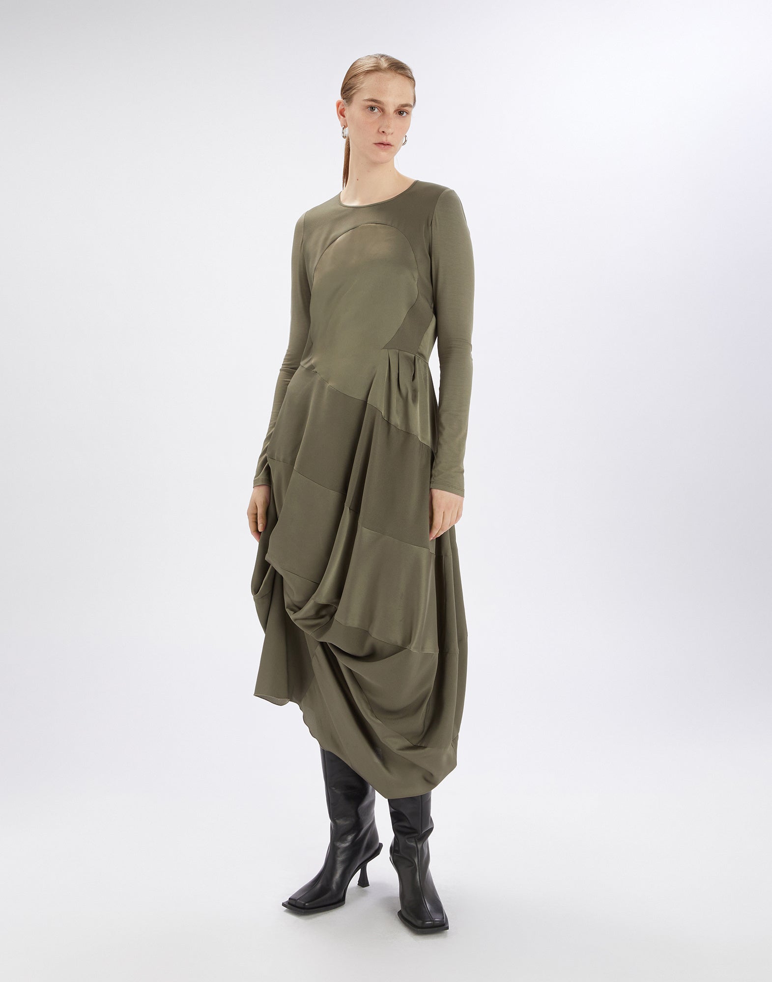 Frontalansicht: Modell trägt das olivgrüne Kleid PLACID aus Stretch-Viskosejersey mit langen Ärmeln, rundem Ausschnitt und drapiertem, glänzendem Polyestersatinrock.