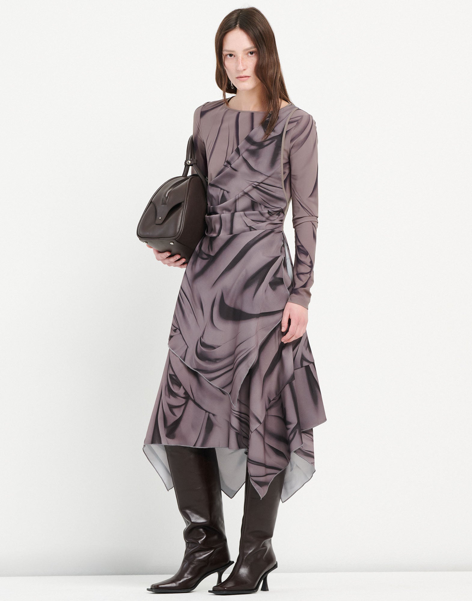 Frontalansicht: TROUPE Kleid mit abstraktem Drapery-Muster, langen Ärmeln, rundem Ausschnitt und asymmetrischem Saum, getragen von Model mit kniehohen Stiefeln.
