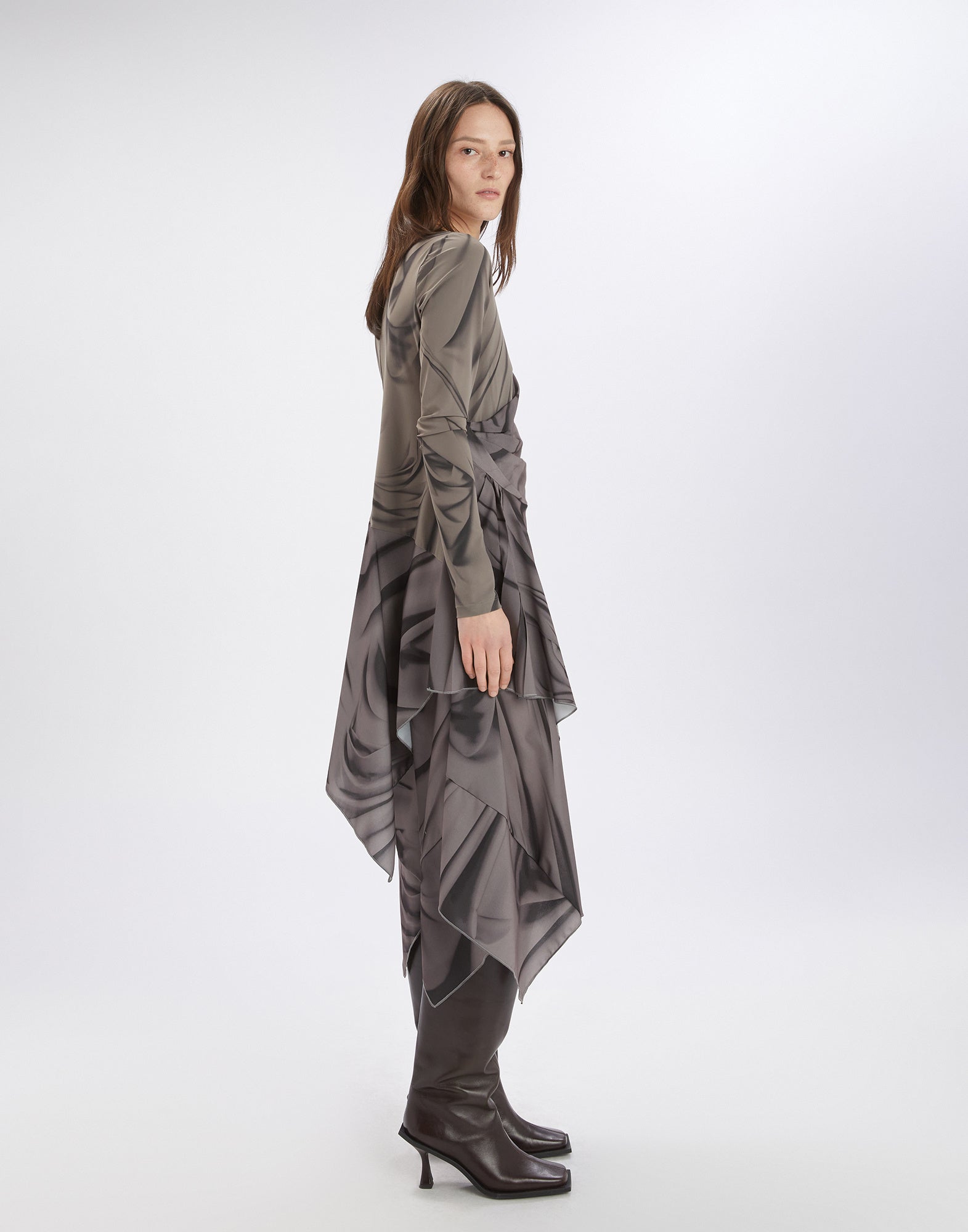Side view of the TROUPE dress worn by a woman. The long dress features an artistic drapery pattern, asymmetric hem, and long sleeves, falling lightly and unlined.